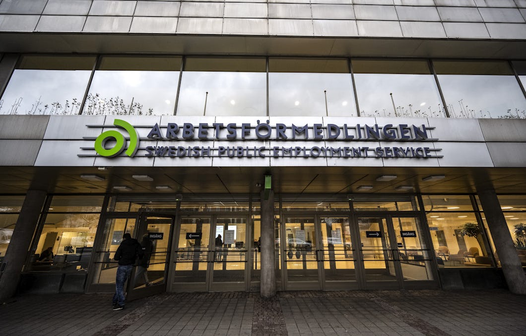Ingången till ett av Arbetsförmedlingens kontor med glasdörrar, skylt och en person som står utanför.