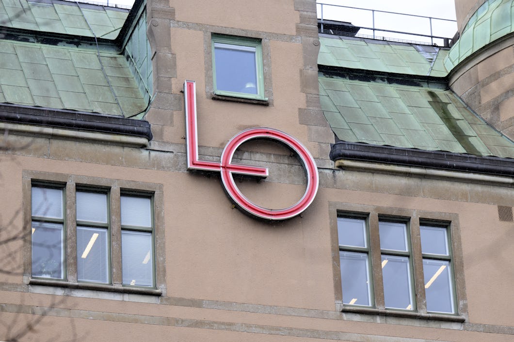 En byggnadsfasad med takpannor i grönt och en stor röd "LO"-logotyp placerad mellan två fönsterrader.