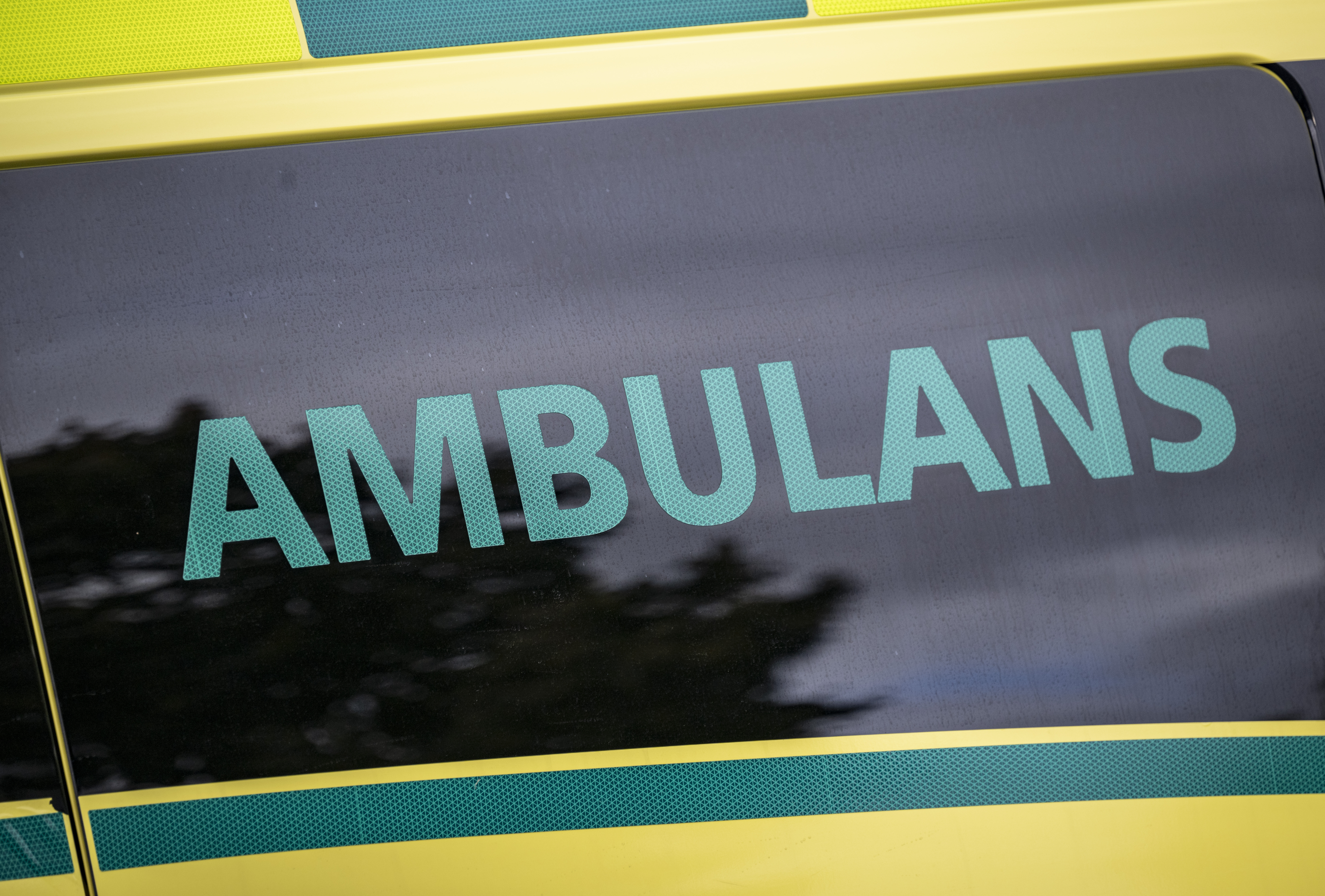 Närbild på en gul ambulans med ordet "AMBULANS" i turkos text på rutan.