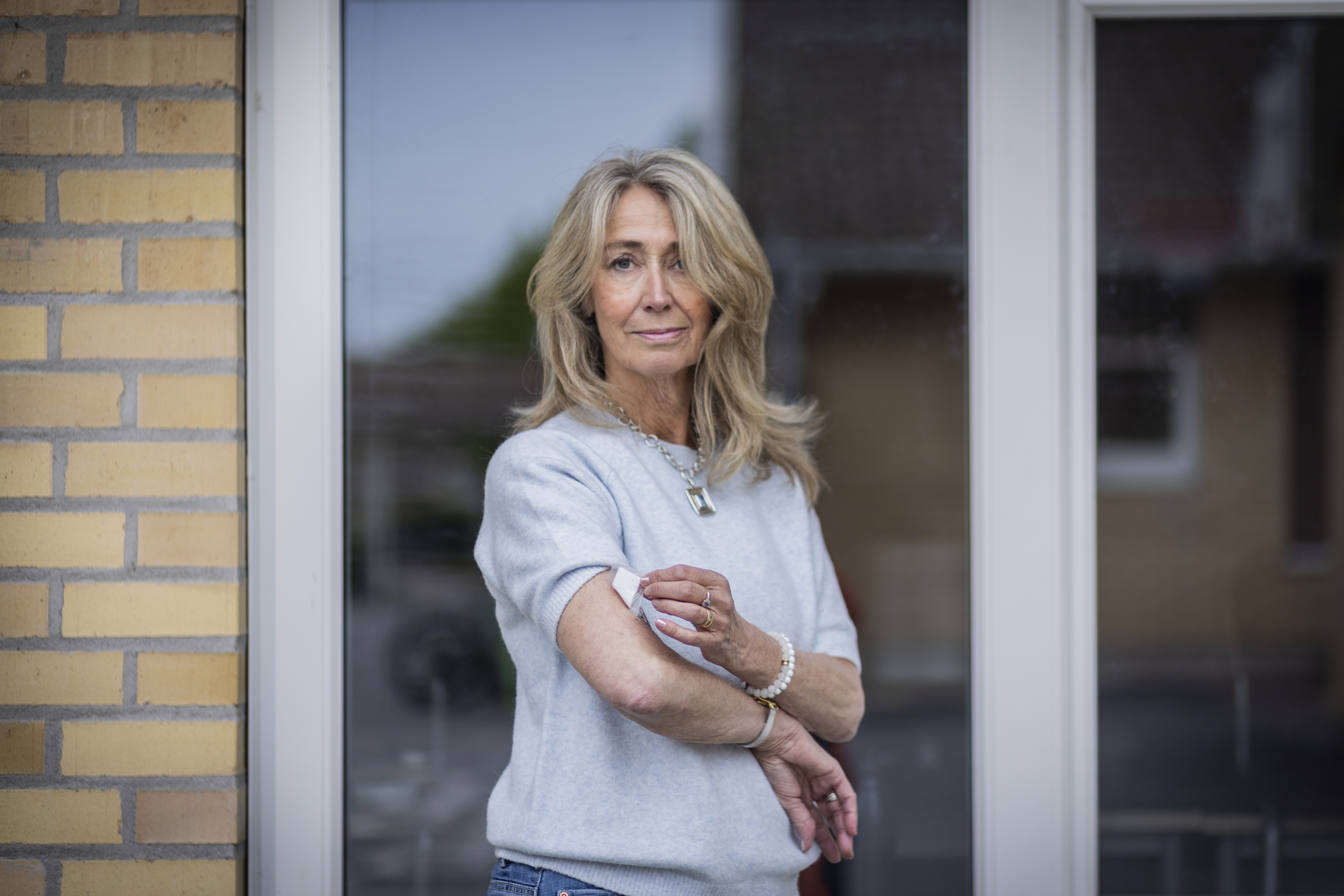 Birgitta Larsson framför ett fönster med ett hormonplåster på ena armen.