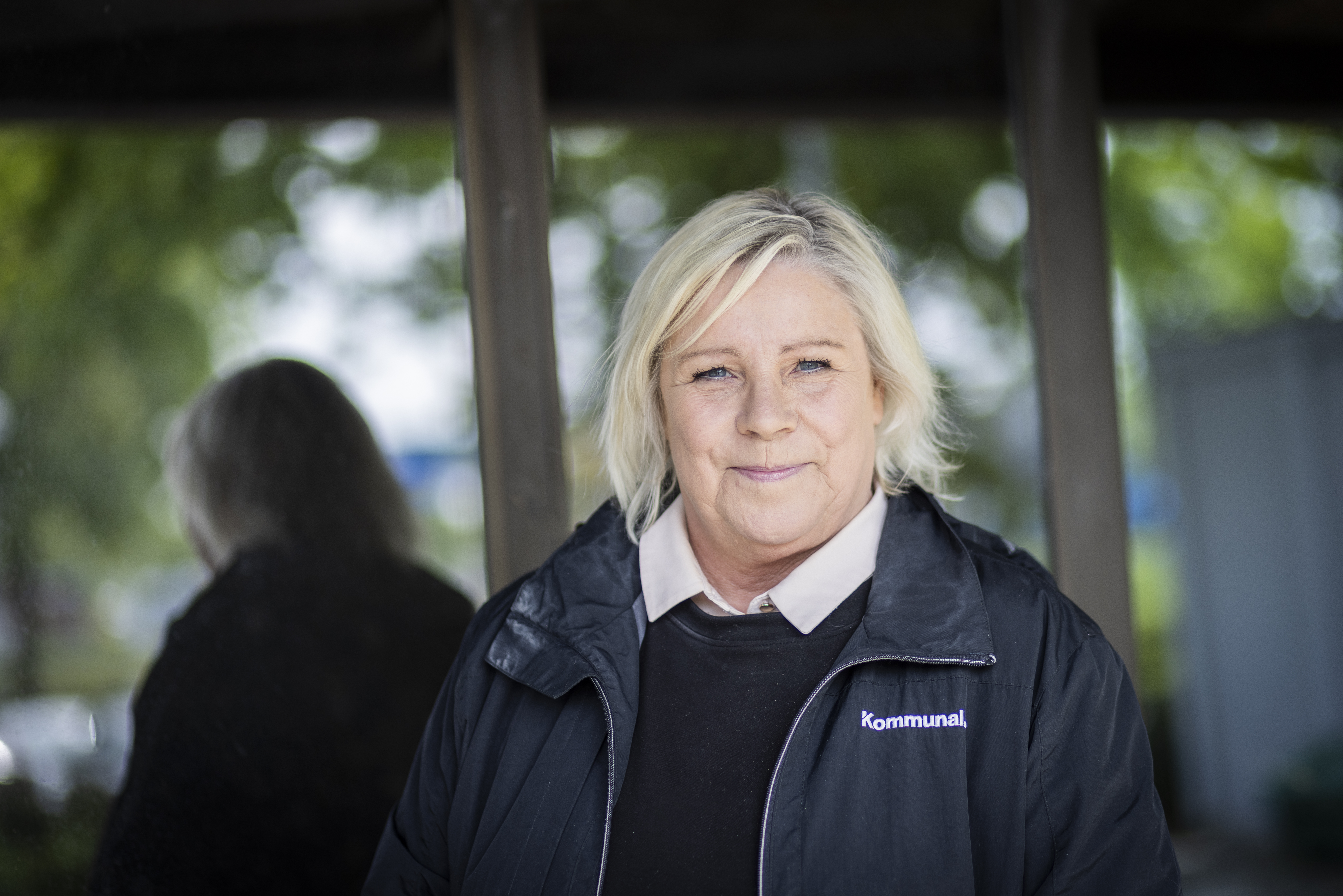 Katarina Brännström med blont hår i en svart Kommunal-jacka står framför en glasruta utomhus.
