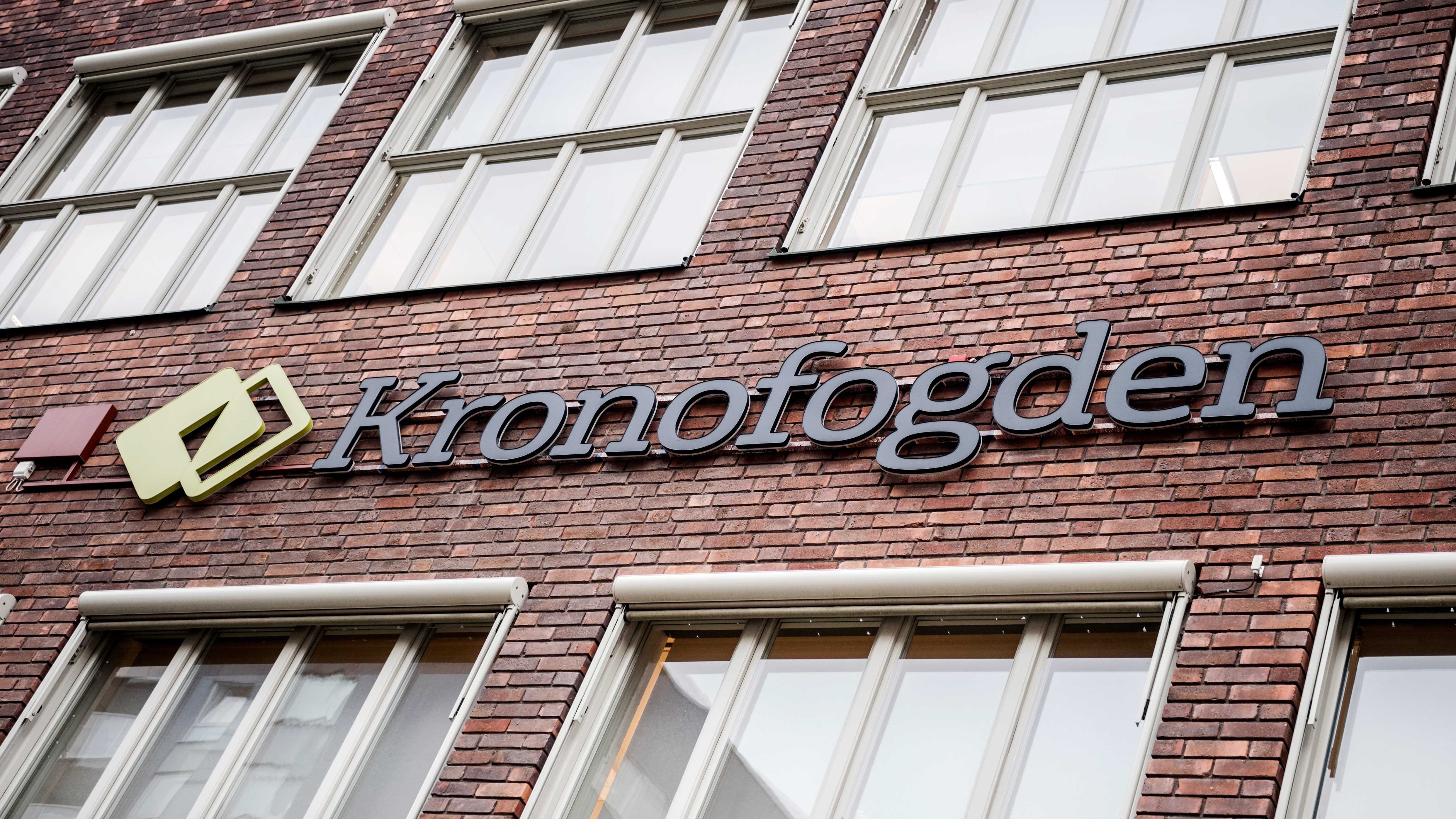 Utsidan av en byggnad i tegel med stora fönster och en skylt där det står "Kronofogden".