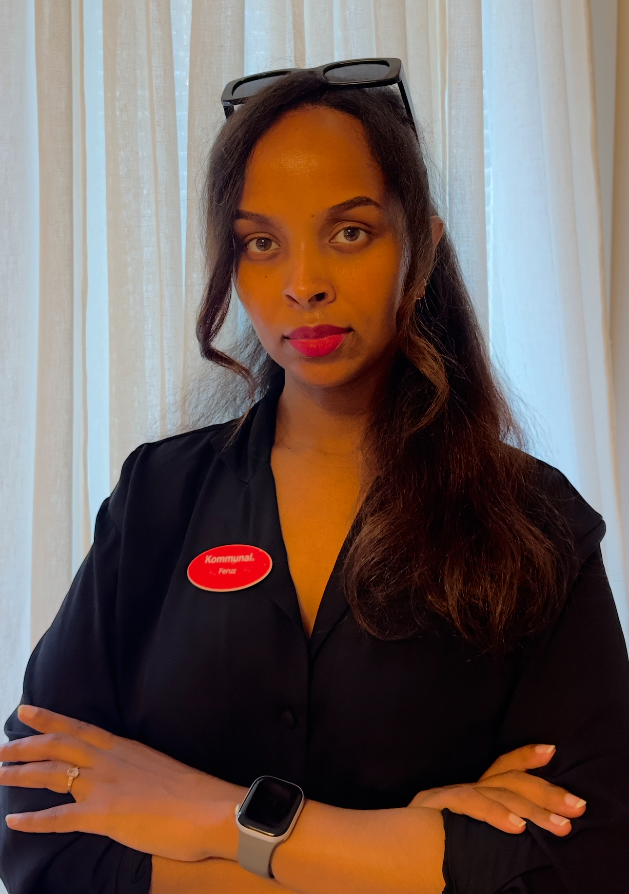 En kvinna med långt mörkt hår kollar in i kameran med allvarlig blick. Hennes armar är korsade över bröstet. På tröjan sitter en skylt med Kommunals logotyp.