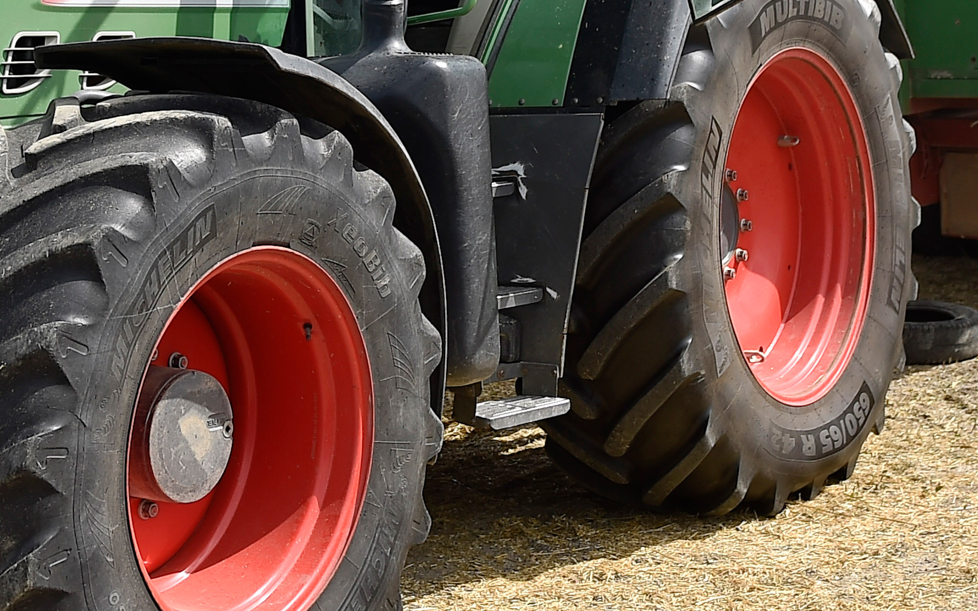 Närbild av bak- och framhjul på en grön traktor med svarta däck och röda fälgar, parkerad på en jordyta.