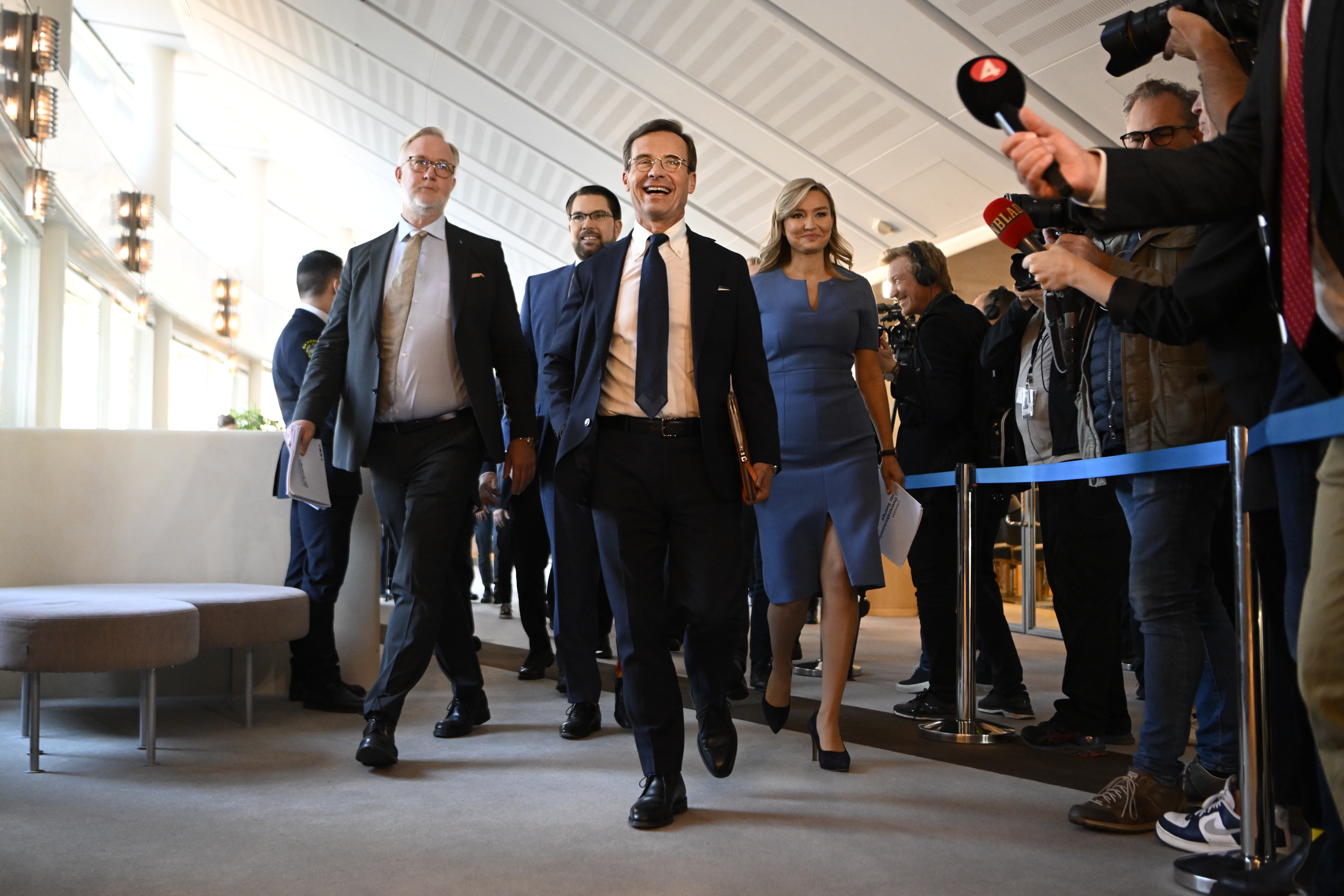 Johan Pehrson (L), Jimmie Åkesson (SD), Ulf Kristersson (M) och Ebba Busch (KD) går i riksdagskorridor omgivna av journalister.