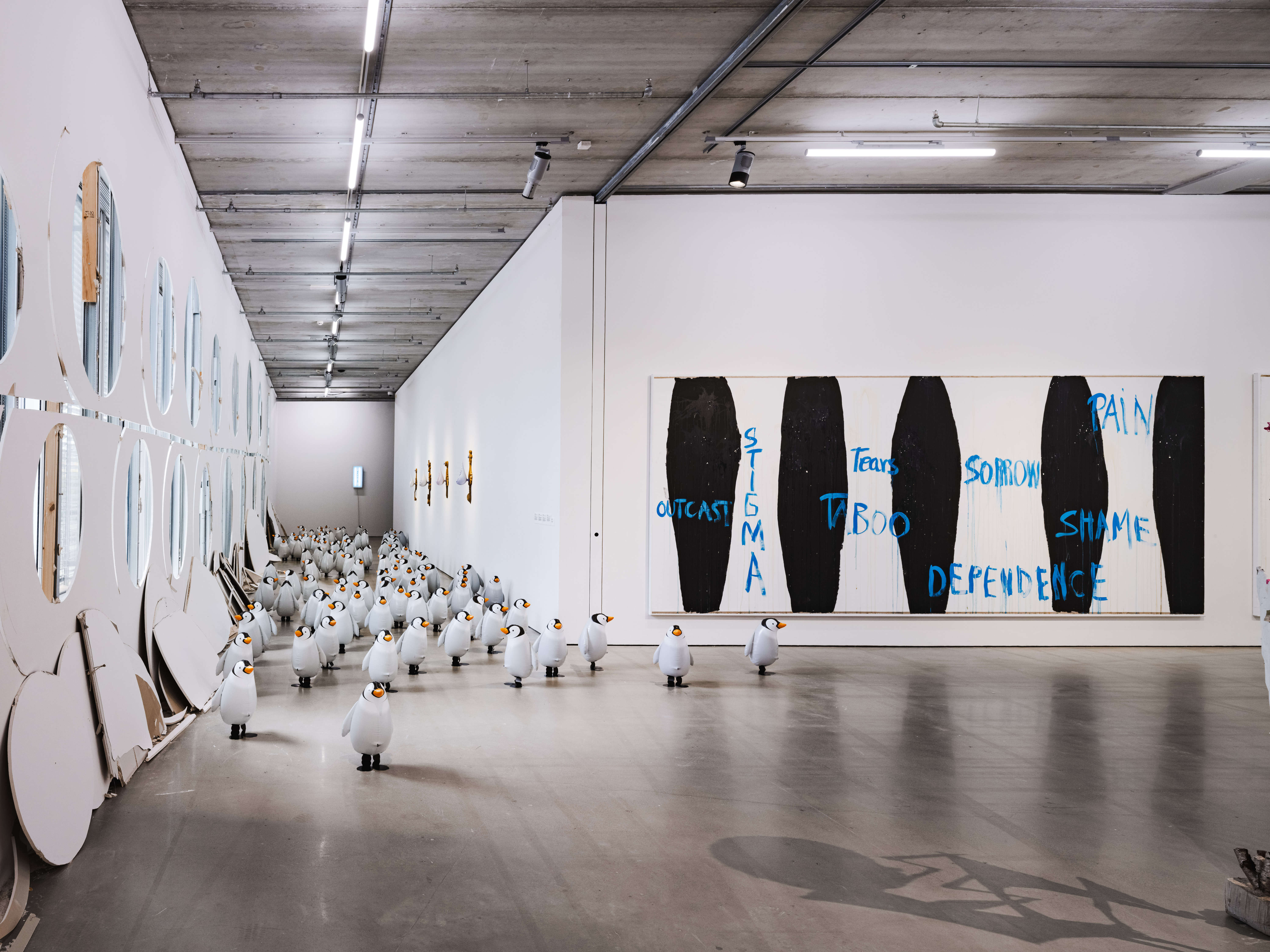 Konstgalleri med flera pingvinskulpturer på golvet, trasiga runda speglar på vänstra väggen och en tavla med text på högra väggen.