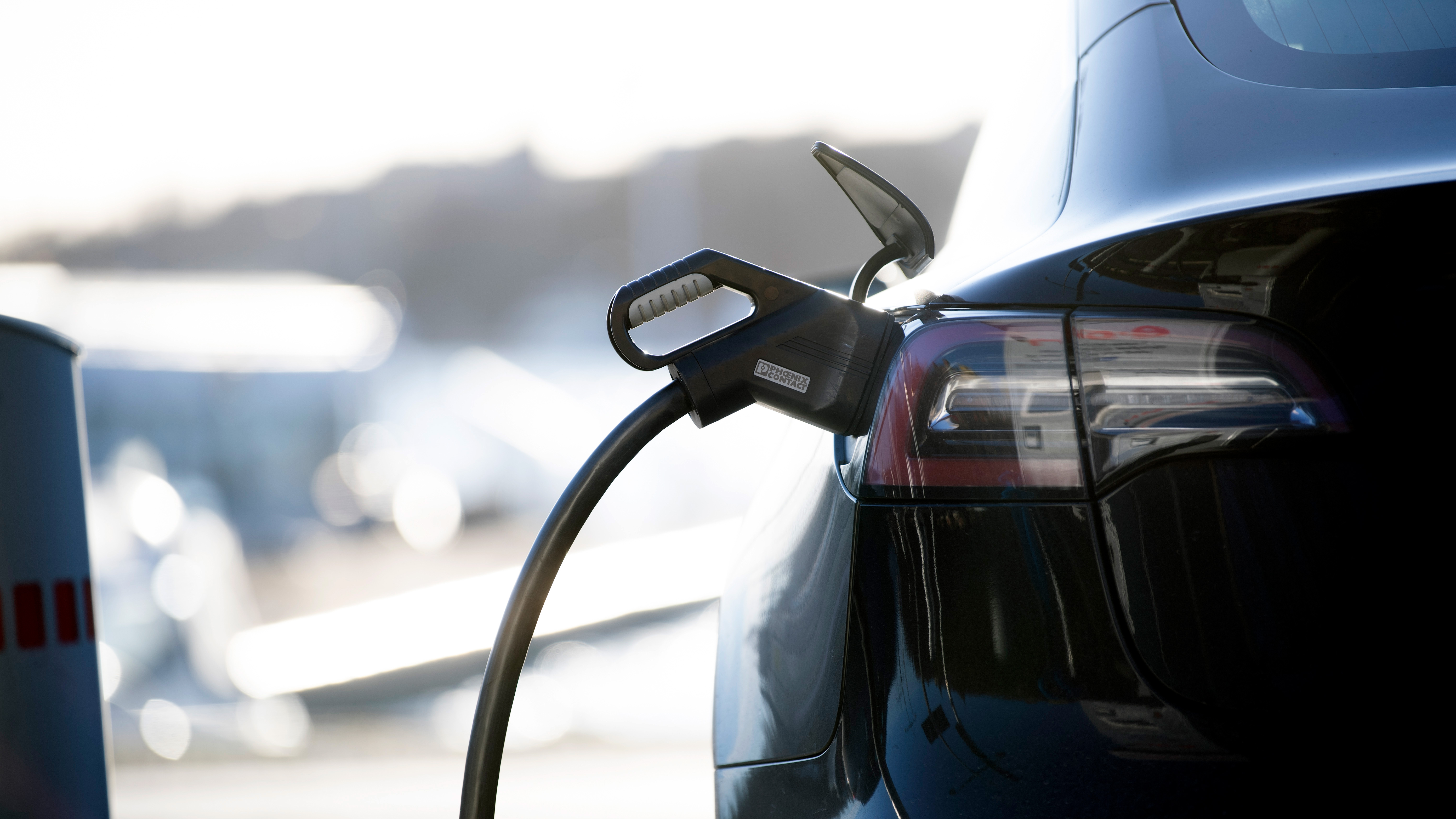 En svart elbil är ansluten till en laddstation, med laddkabeln kopplad till bilens uttag.