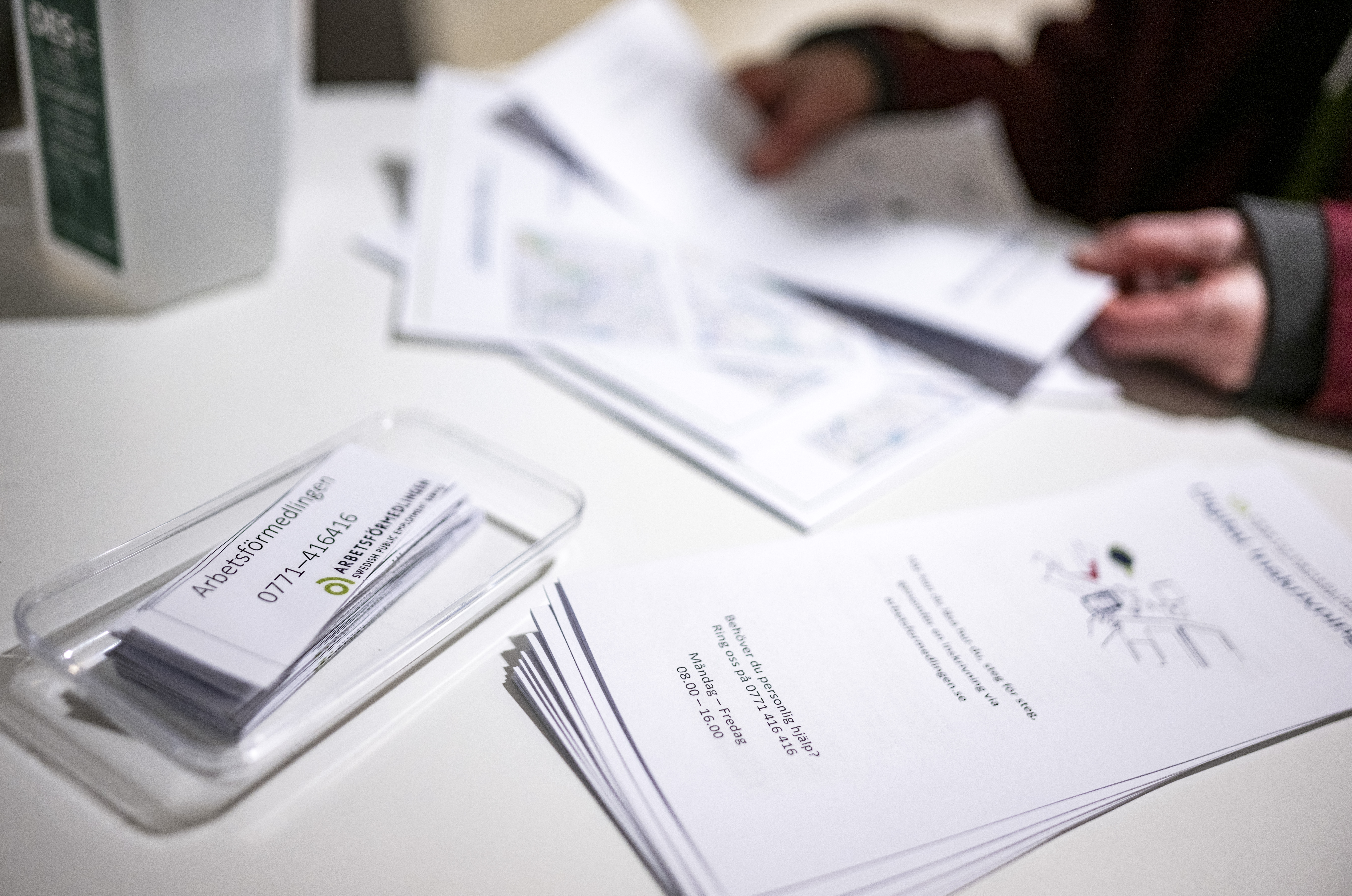 En person sitter vid ett bord med informationsblad och visitkort från Arbetsförmedlingen.