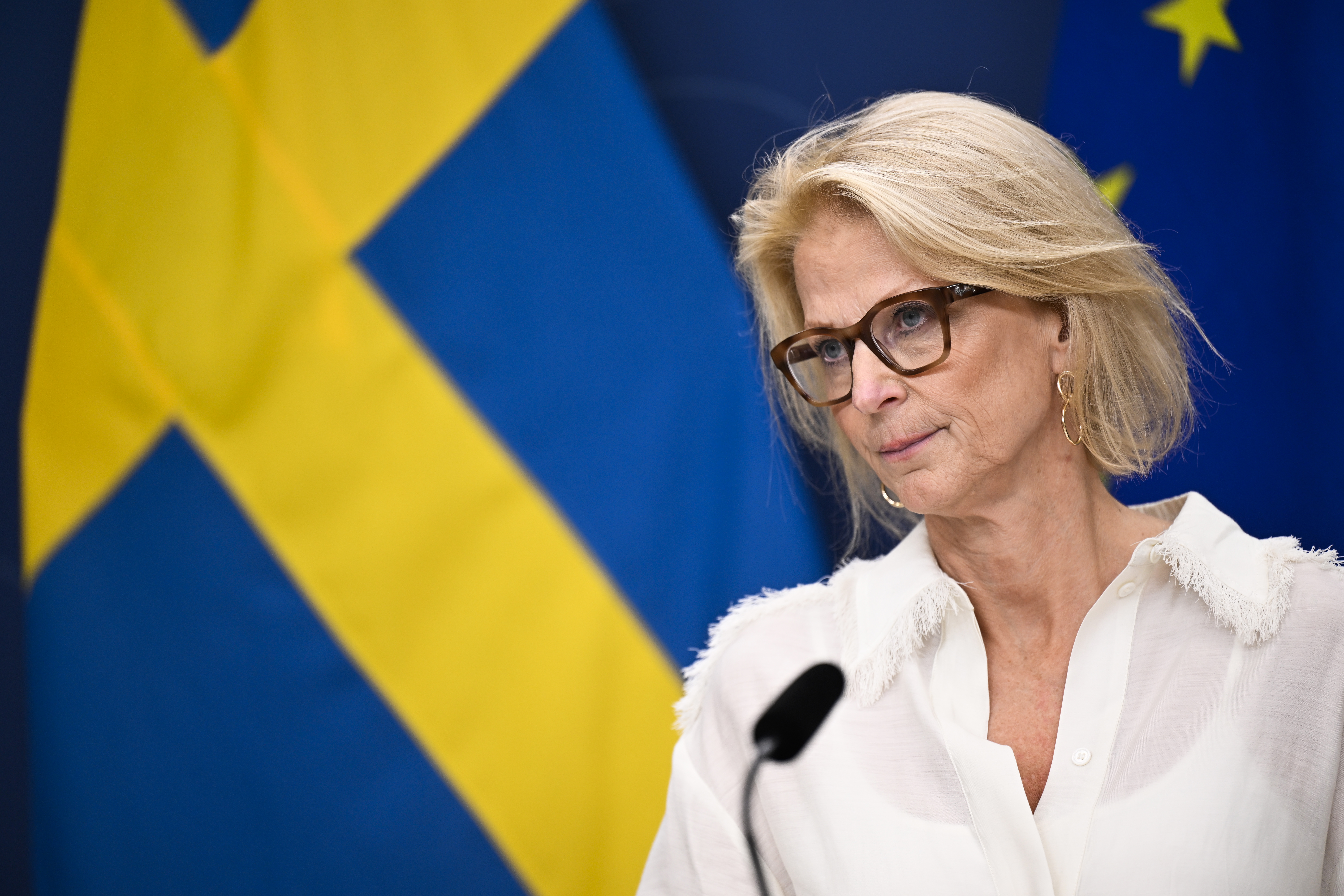 Finansminister Svantesson (M), klädd i vit blus står vid ett podium med Sveriges och Europeiska unionens flaggor i bakgrunden.