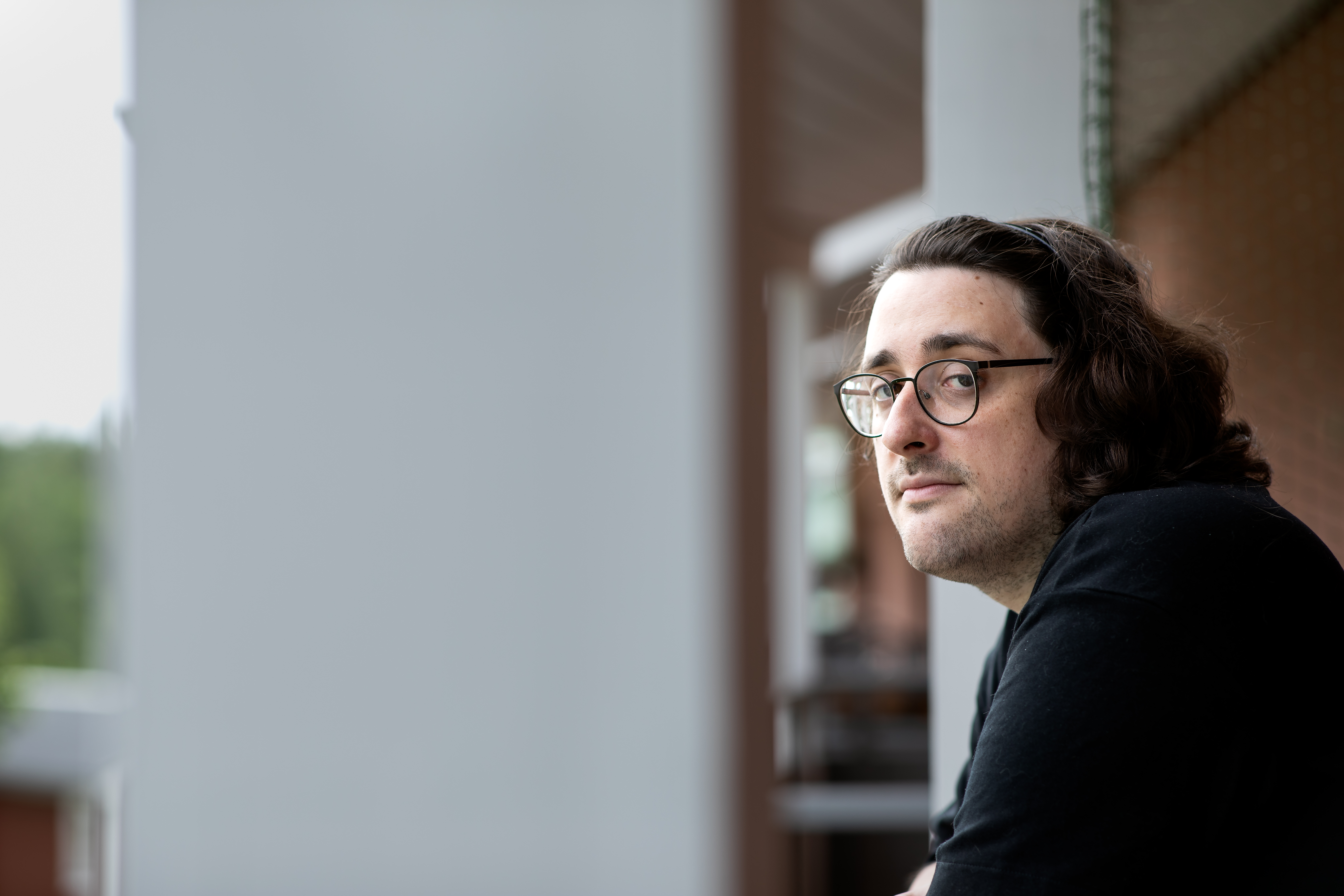 Felipe Gaboardi med långt mörkt hår och glasögon, iklädd svart tröja, ser mot kameran och lutar sig mot ett balkongräcke. Bakgrunden är suddig.