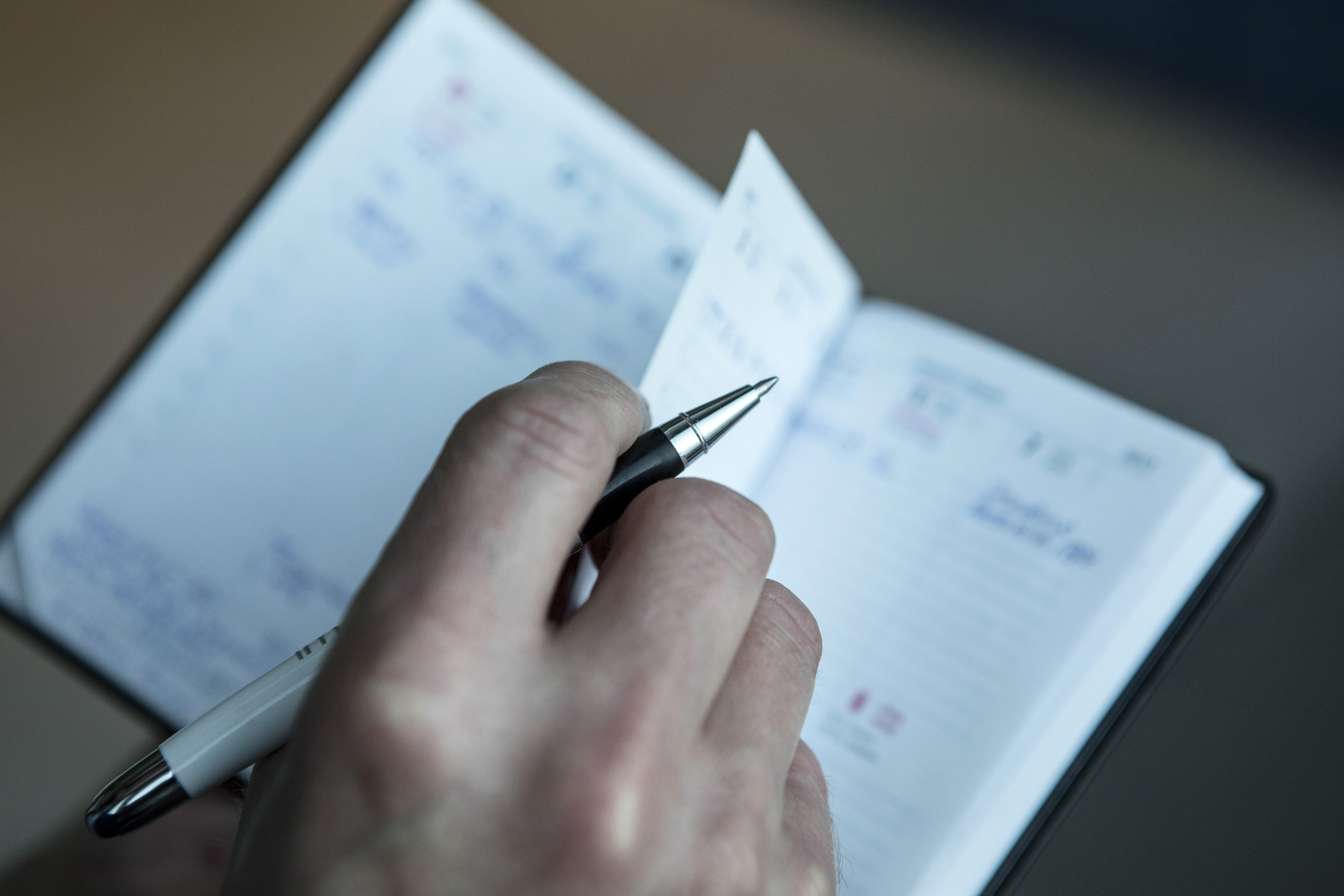 En person håller i en penna och bläddrar i sidor av en öppen kalender med handskrivna anteckningar och datum.