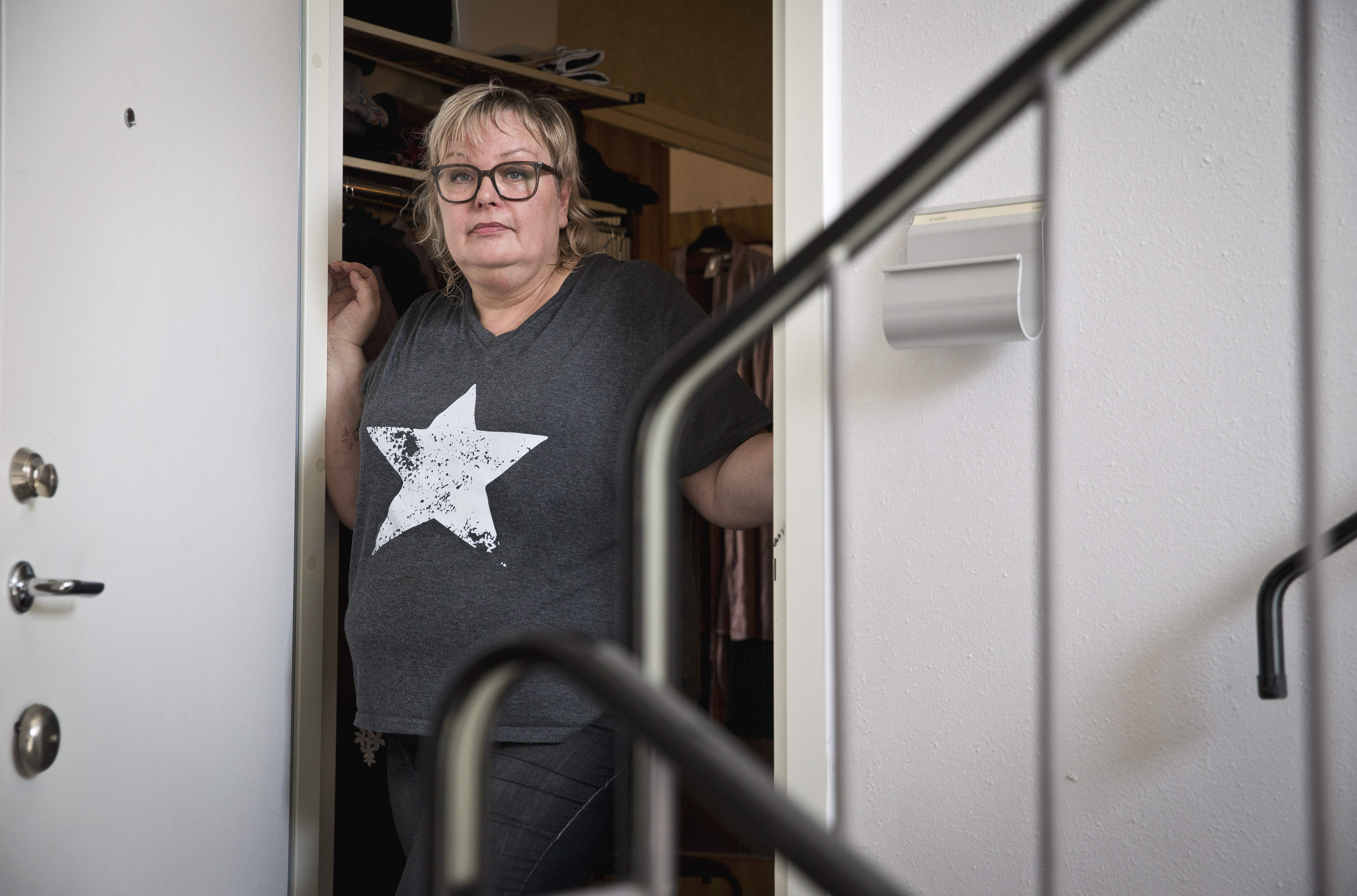 Åsa Skane med glasögon och skjorta med stjärntryck står i en dörröppning och håller i dörrkarmen, en trappa syns framför.