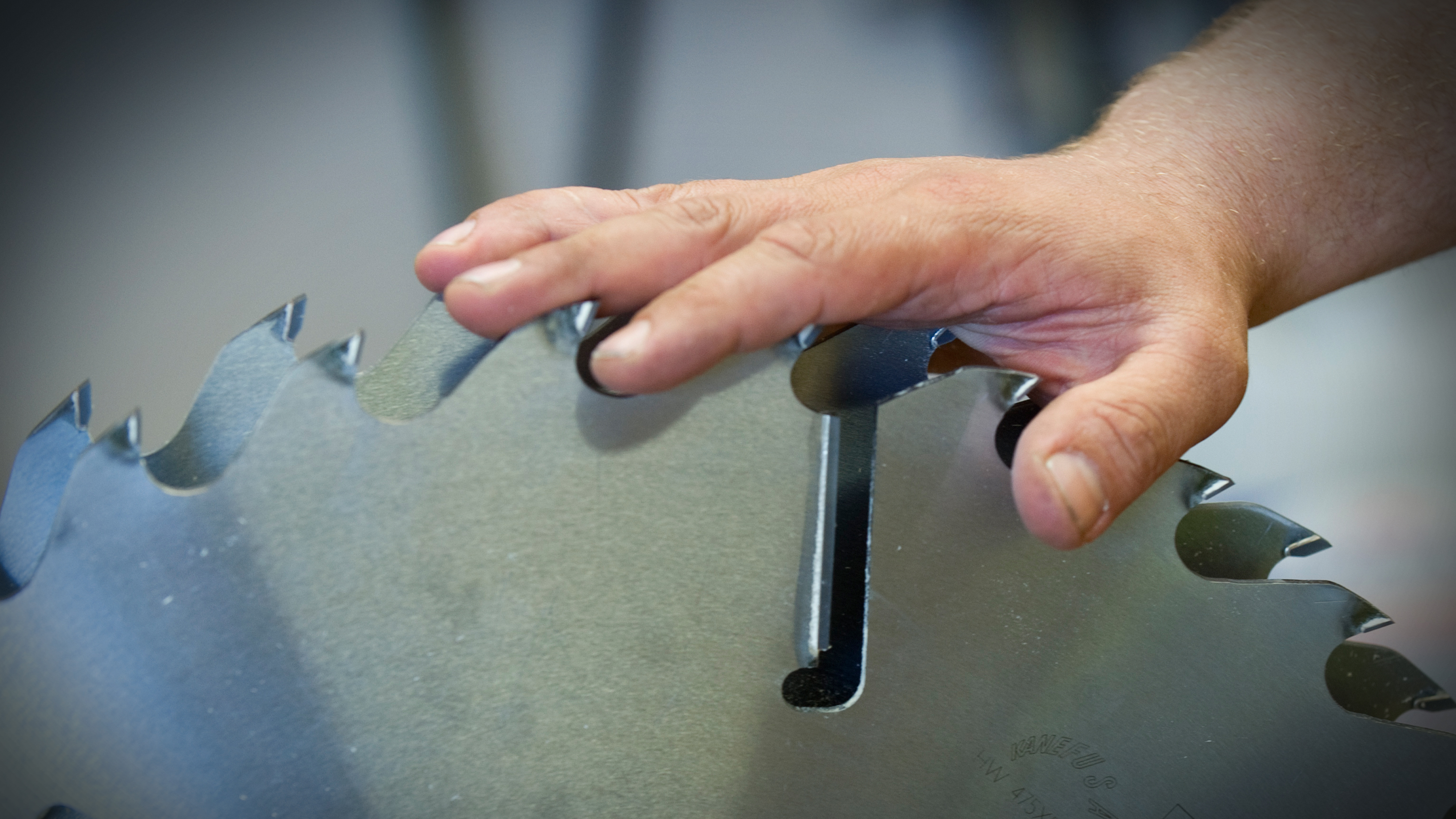 En hand rör vid en stor cirkelsågs vassa tänder, vilket visar risken för skada.