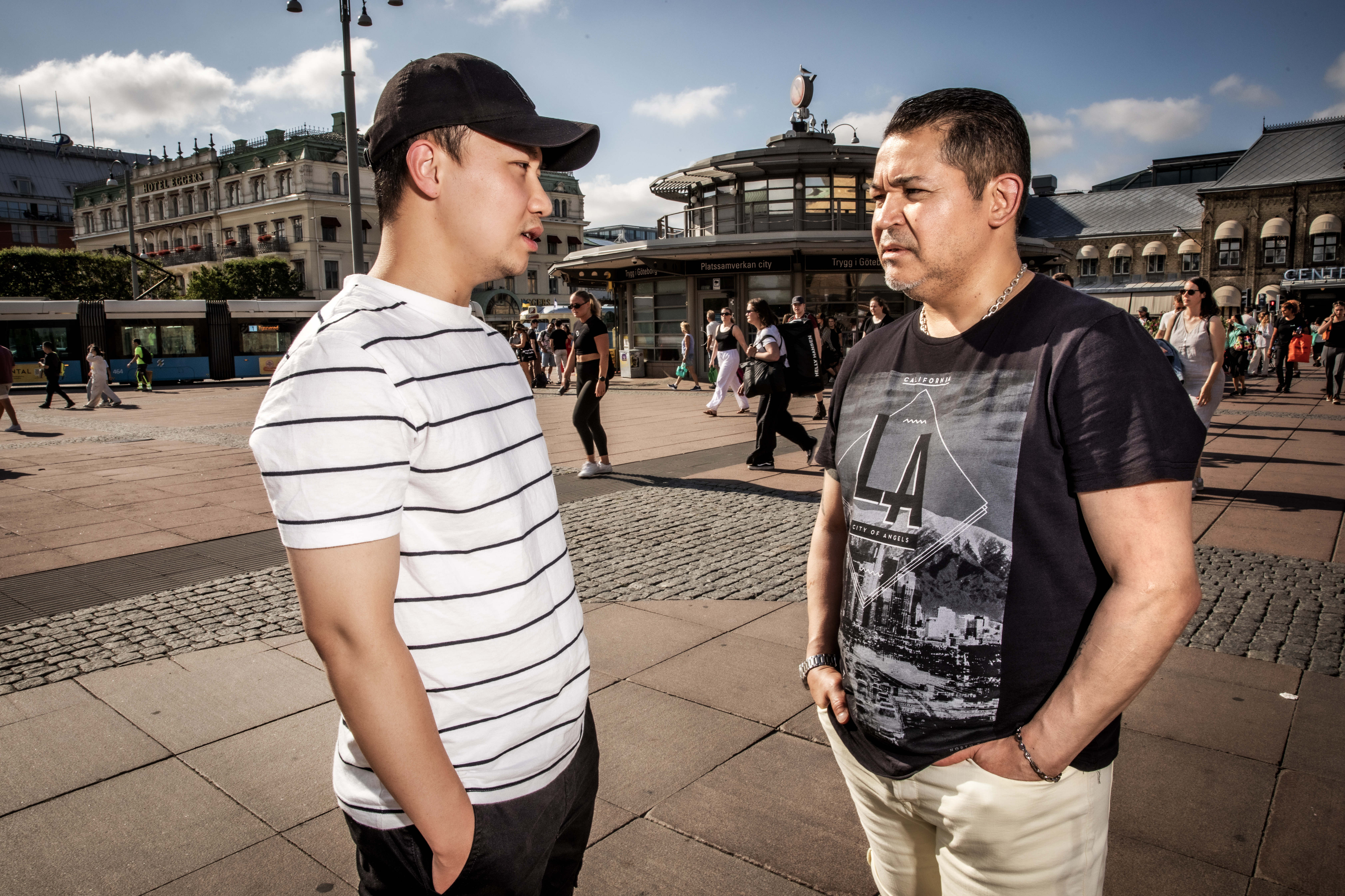 Le Loc Nguyen och Antonio Isla står vända mot varandra och pratar på stan i Göteborg, med människor som går i bakgrunden.