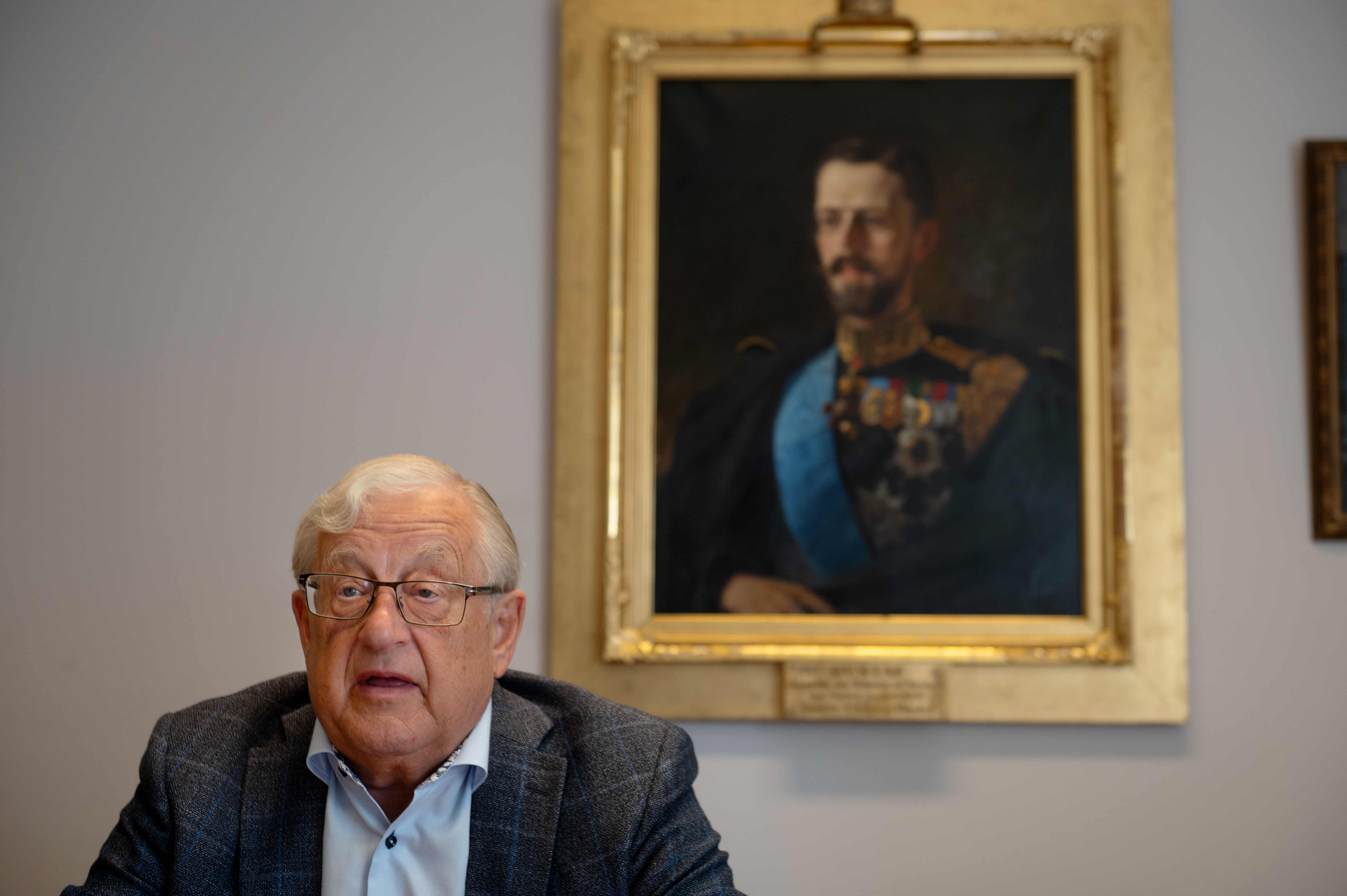 Gustav Svensson med glasögon sitter vid ett skrivbord, bakom honom hänger ett inramat porträtt av Gustav V i militäruniform.