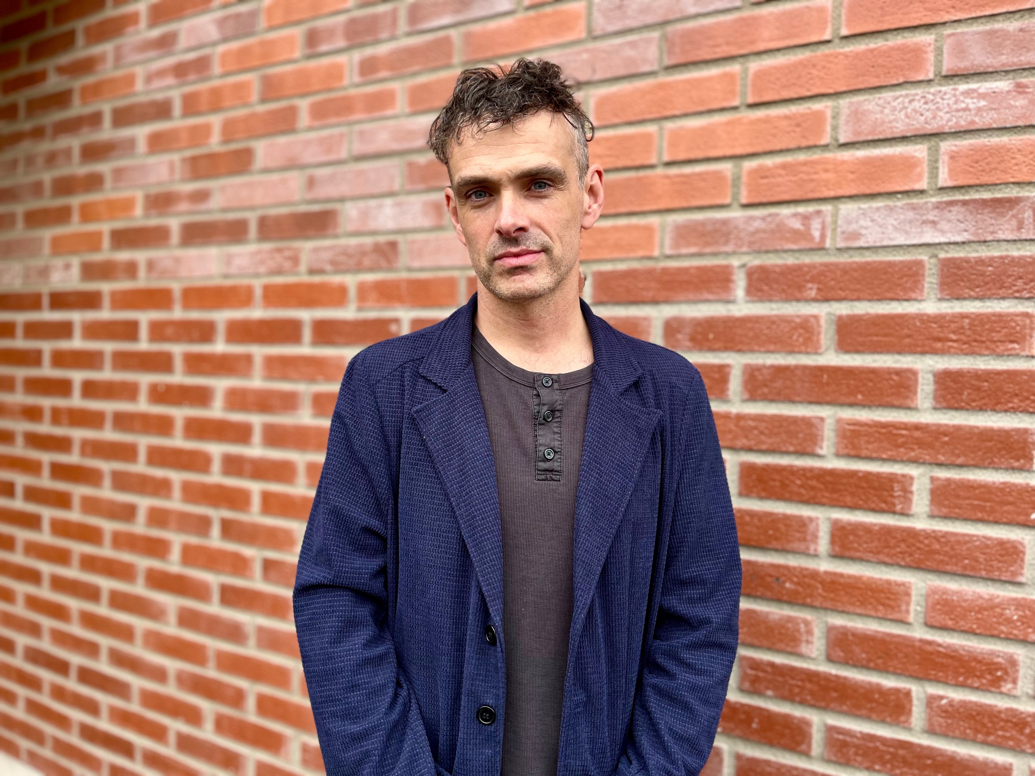 Man i blå kavaj står framför tegelvägg.