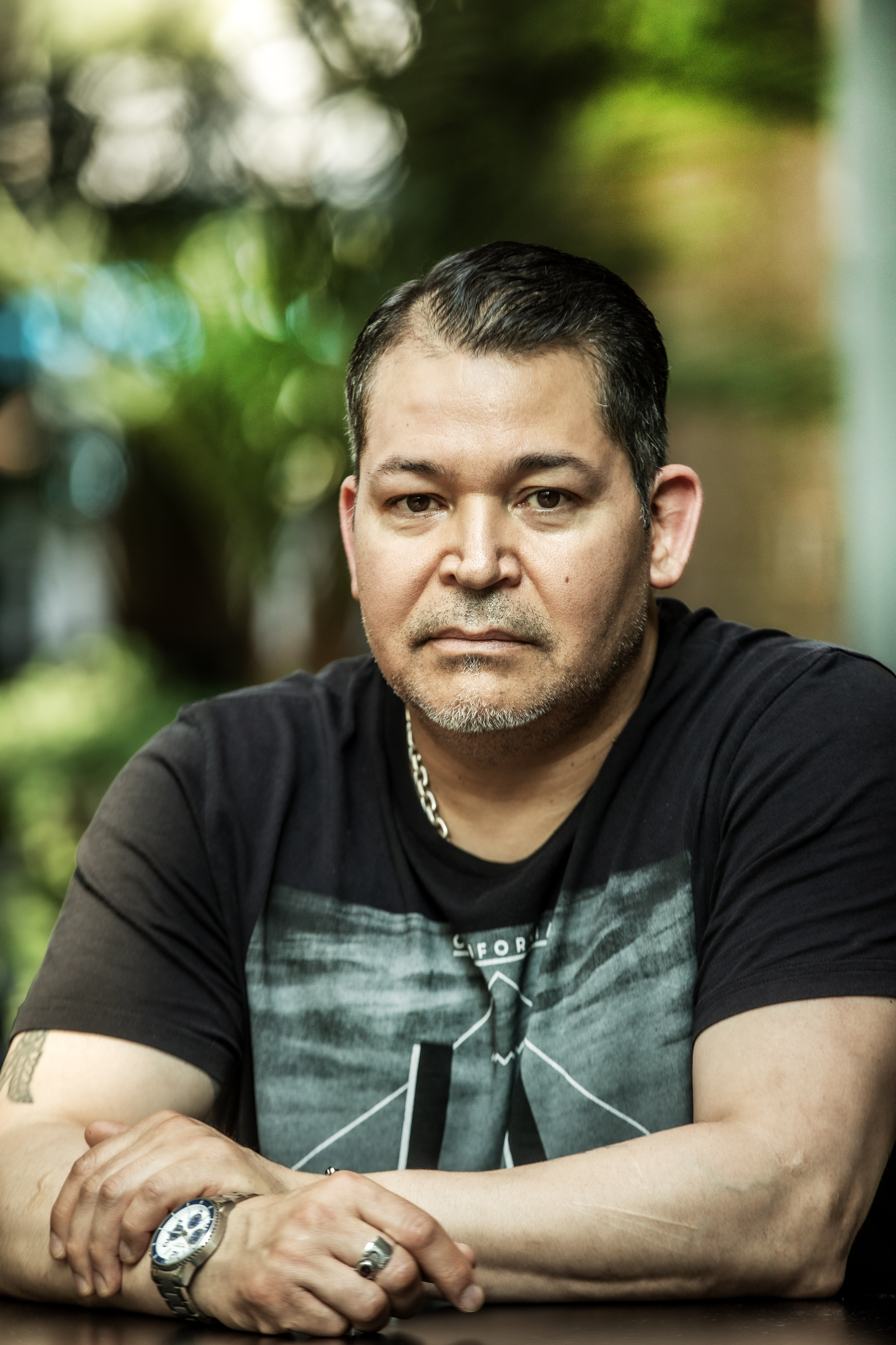 Antonio Isla med kort mörkt hår och skägg sitter vid ett bord utomhus, har svart t-shirt, halskedja, ring och klocka, ser mot kameran.