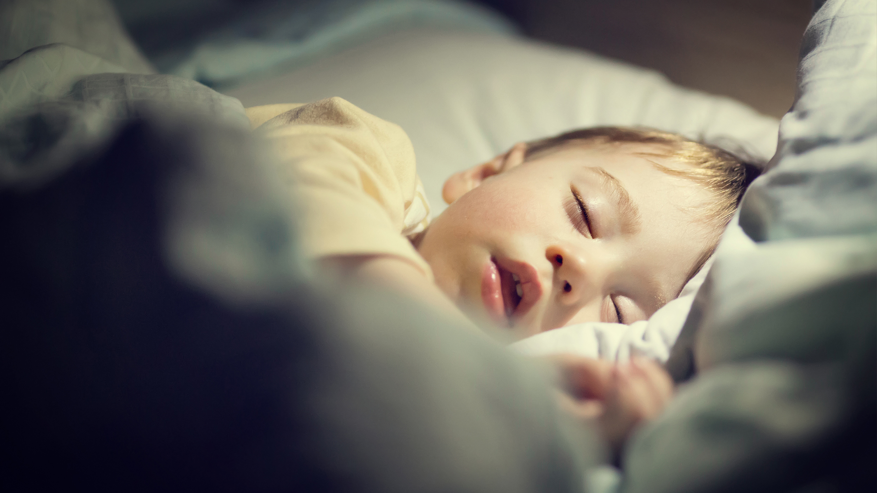 Ett litet barn sover på en säng, med ett huvud på en kudde och ljus som lyser upp ansiktet.