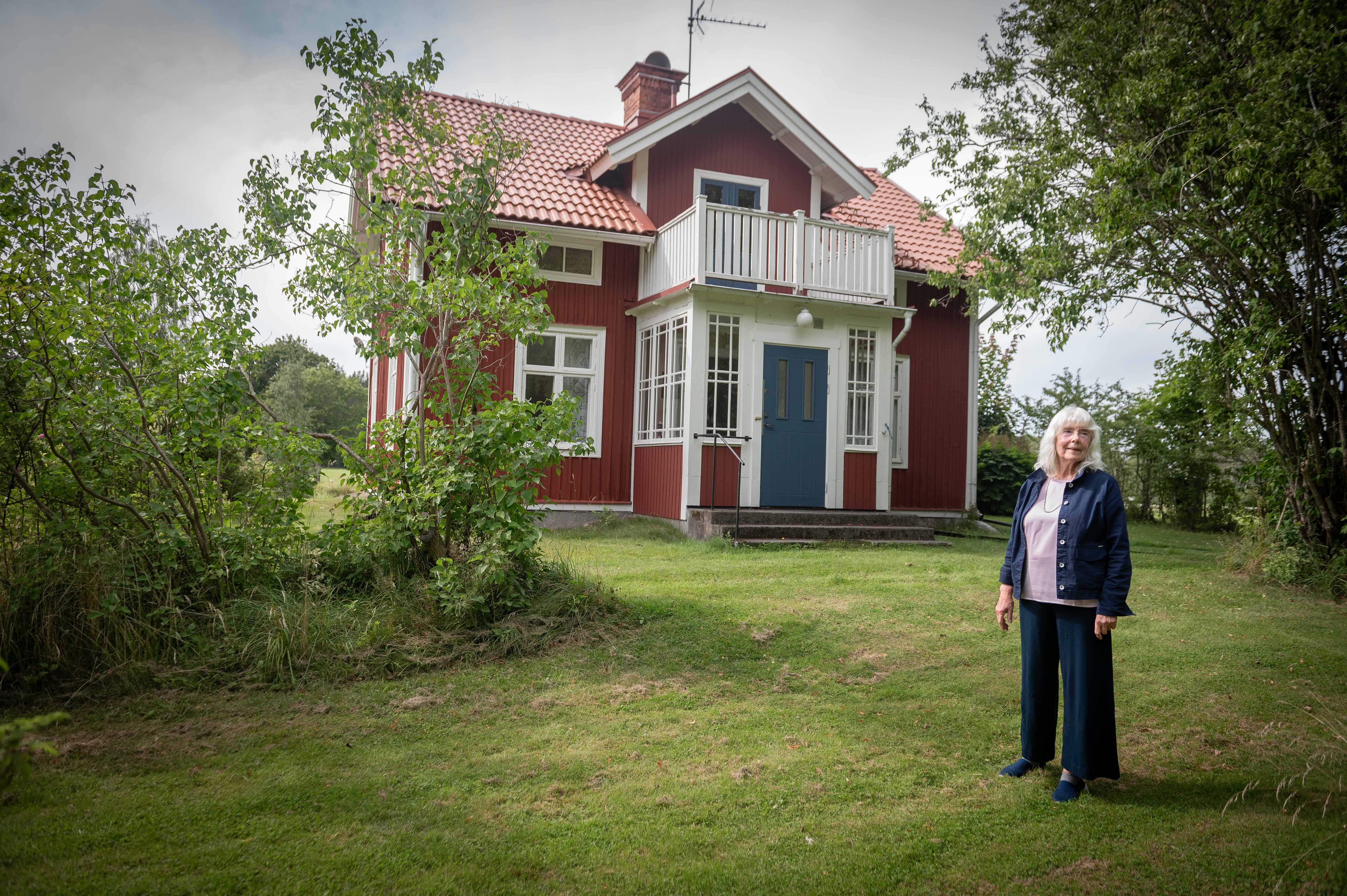 Annette Thörnquist står på gräset framför ett rött och vitt tvåvåningshus med balkong och tegeltak.