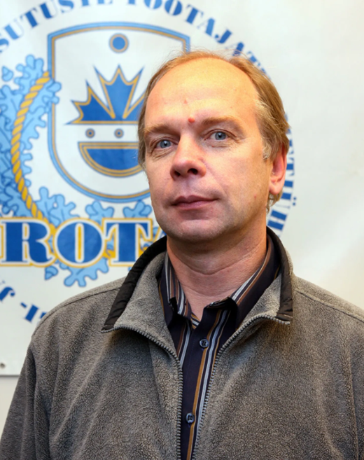 Kalle Liivamägi har en grå fleecejacka och står framför en logotyp på en vägg.