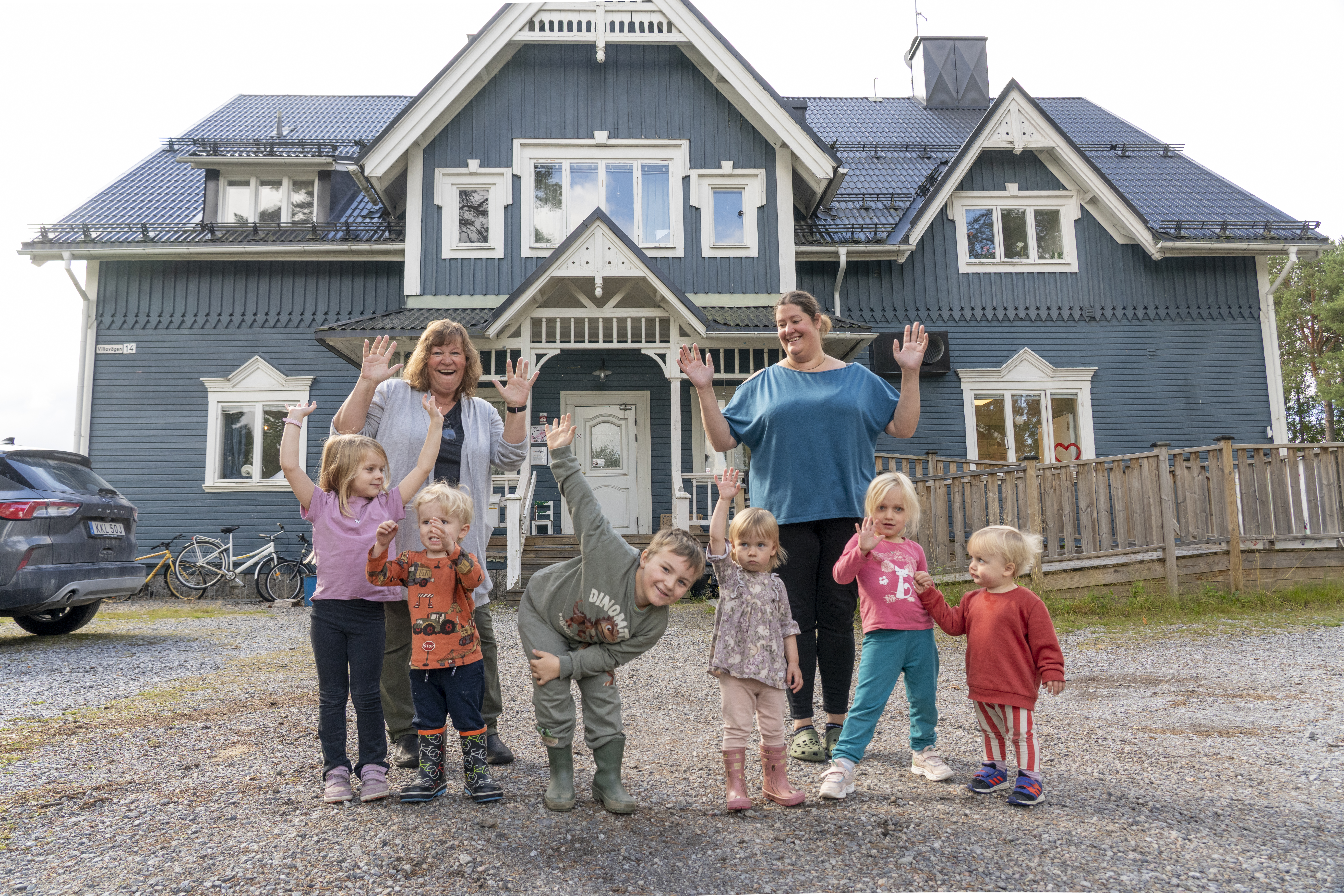 En samling barn och pedagoger framför en stor, blå förskolebyggnad.