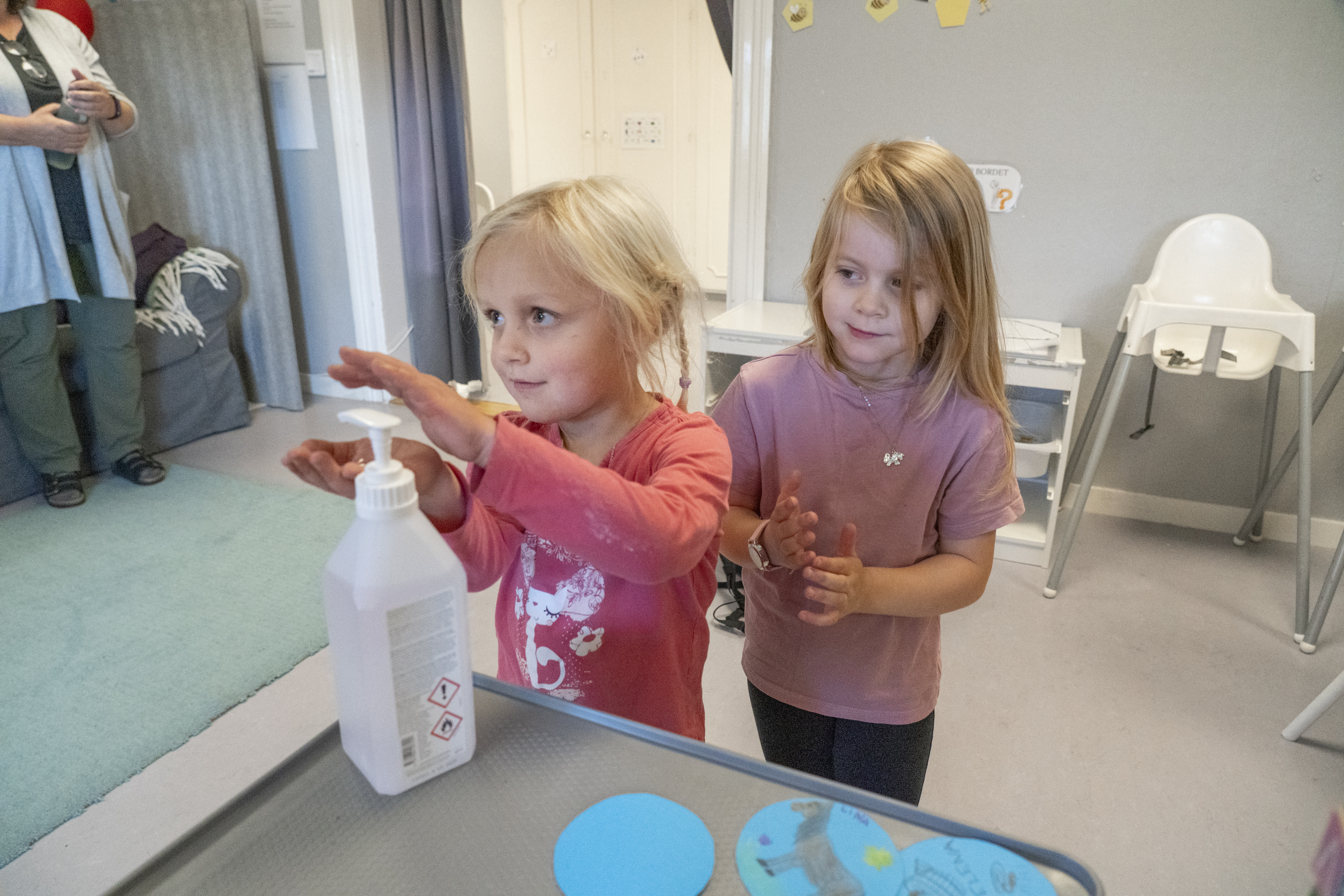 Barnen Tilly och Thelma tvättar händerna, med förskolläraren Helena Sandström i bakgrunden.