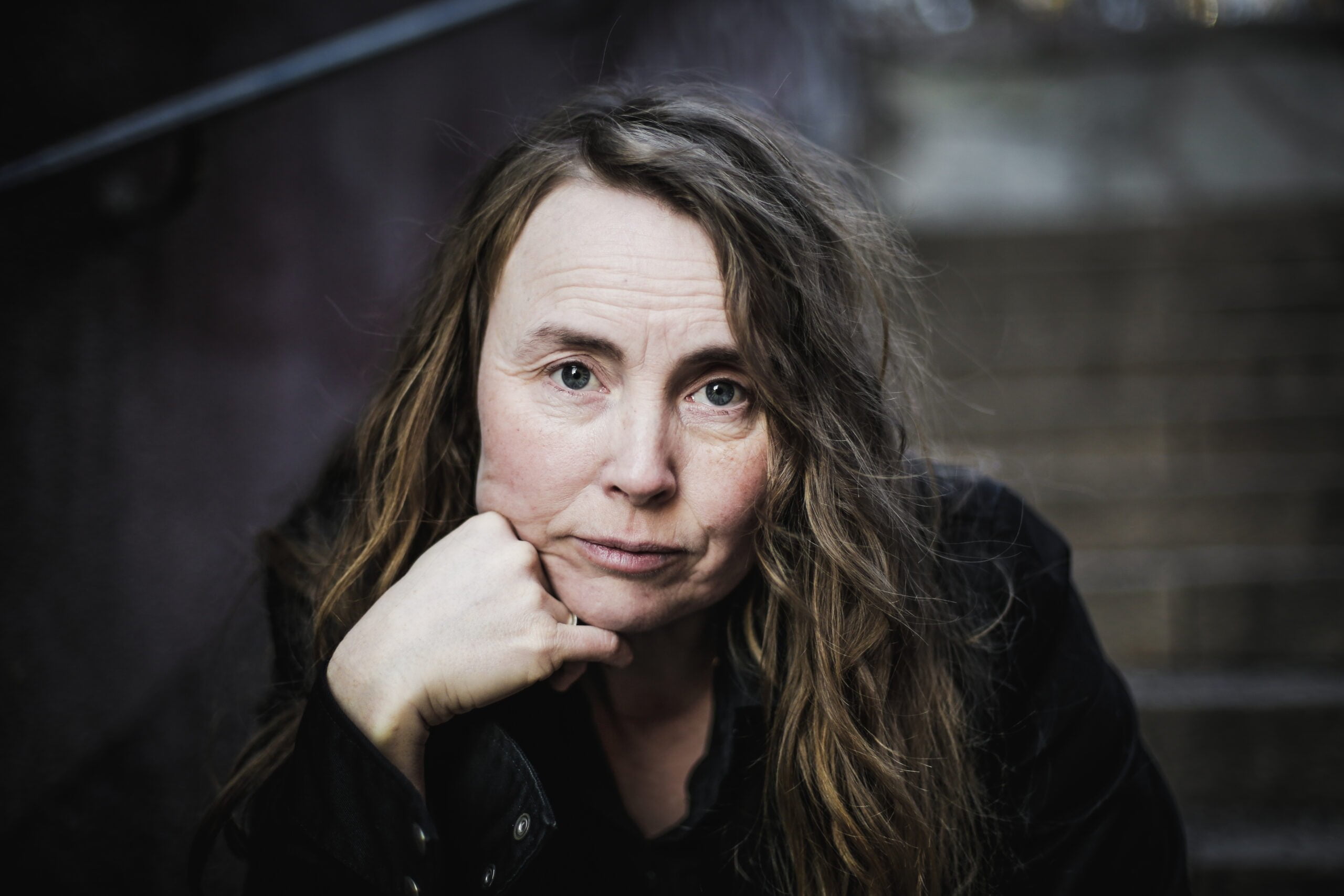 Malin Isaksson, författare, vilar hakan på handen medan hon sitter utomhus nära stensteg.