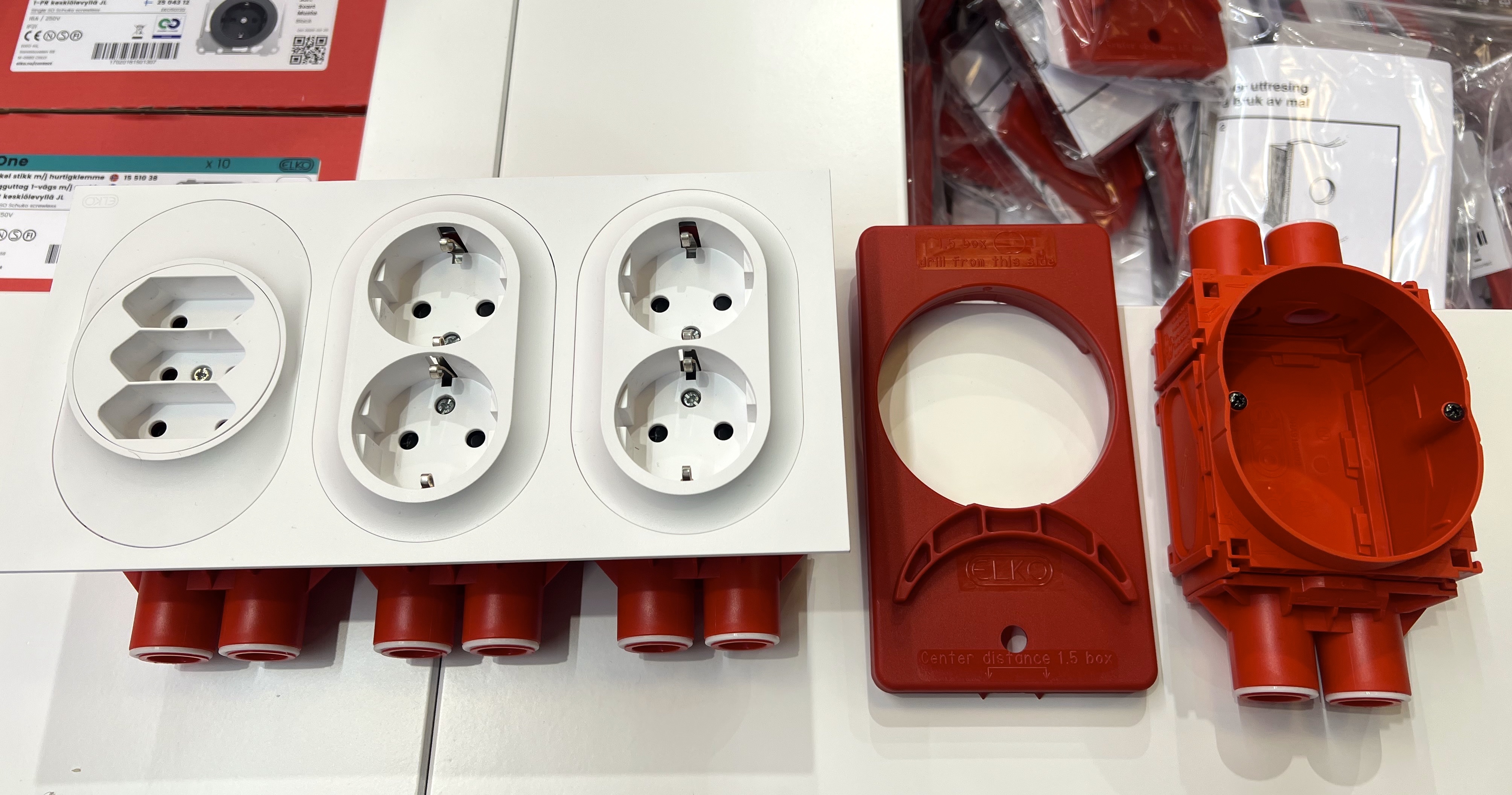 Olika eluttagspaneler och röda monteringsdosor ligger på ett bord och visar olika uttags- och installationsalternativ.