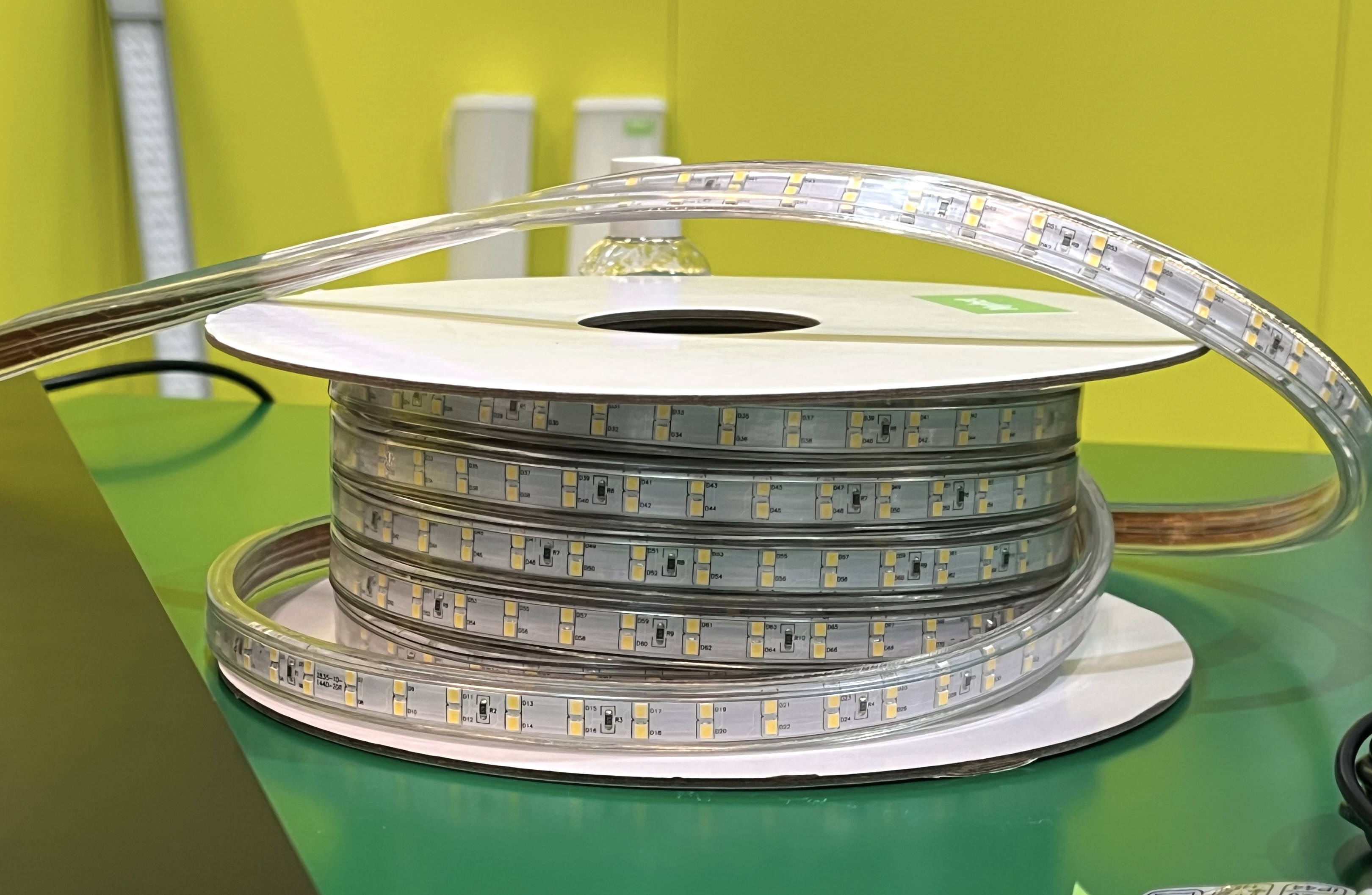 En rulle med LED-ljusremsa ligger på en rund vit spole, placerad på en grön yta med gul bakgrund.