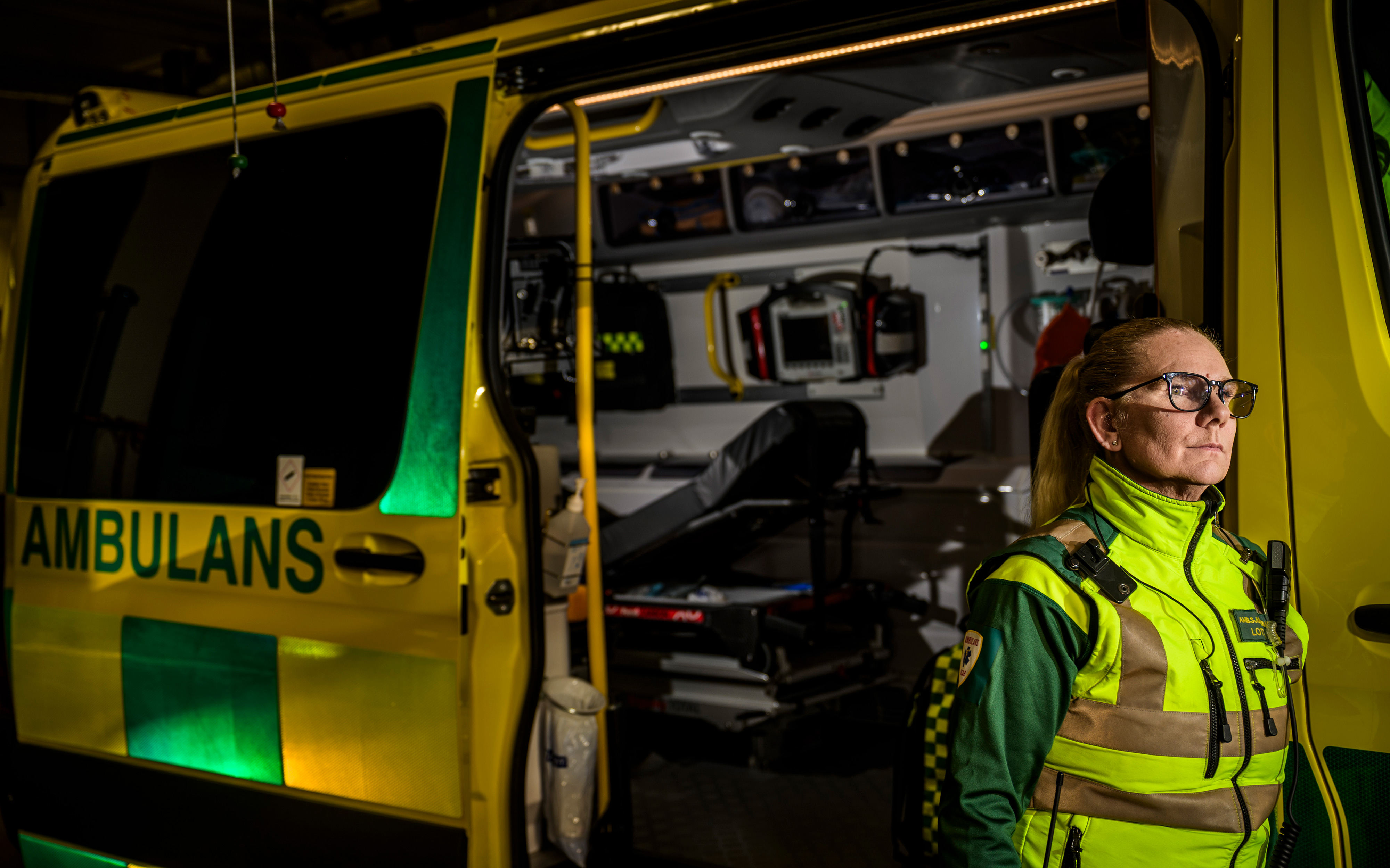 Ambulansarbetaren Lotta Svensson står bredvid en öppen ambulans där medicinsk utrustning syns inuti.