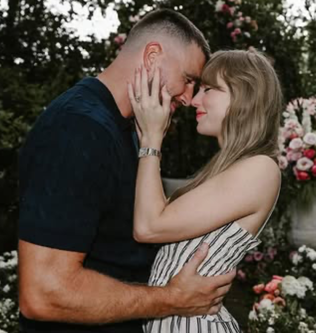 Ett par står nära varandra utomhus, rör vid pannorna och ler, omgivna av blommor och växter.