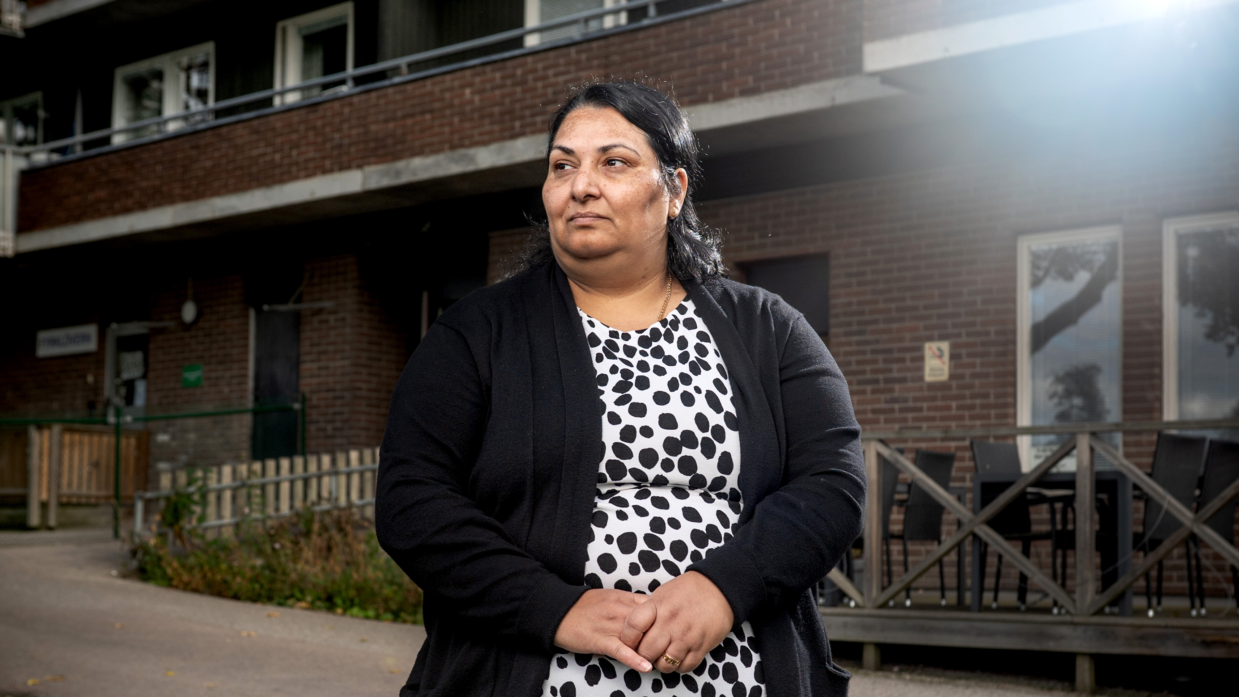 Gjulfidan Saliji i svart kofta och prickig klänning står utanför en tegelbyggnad och tittar lite åt sidan.