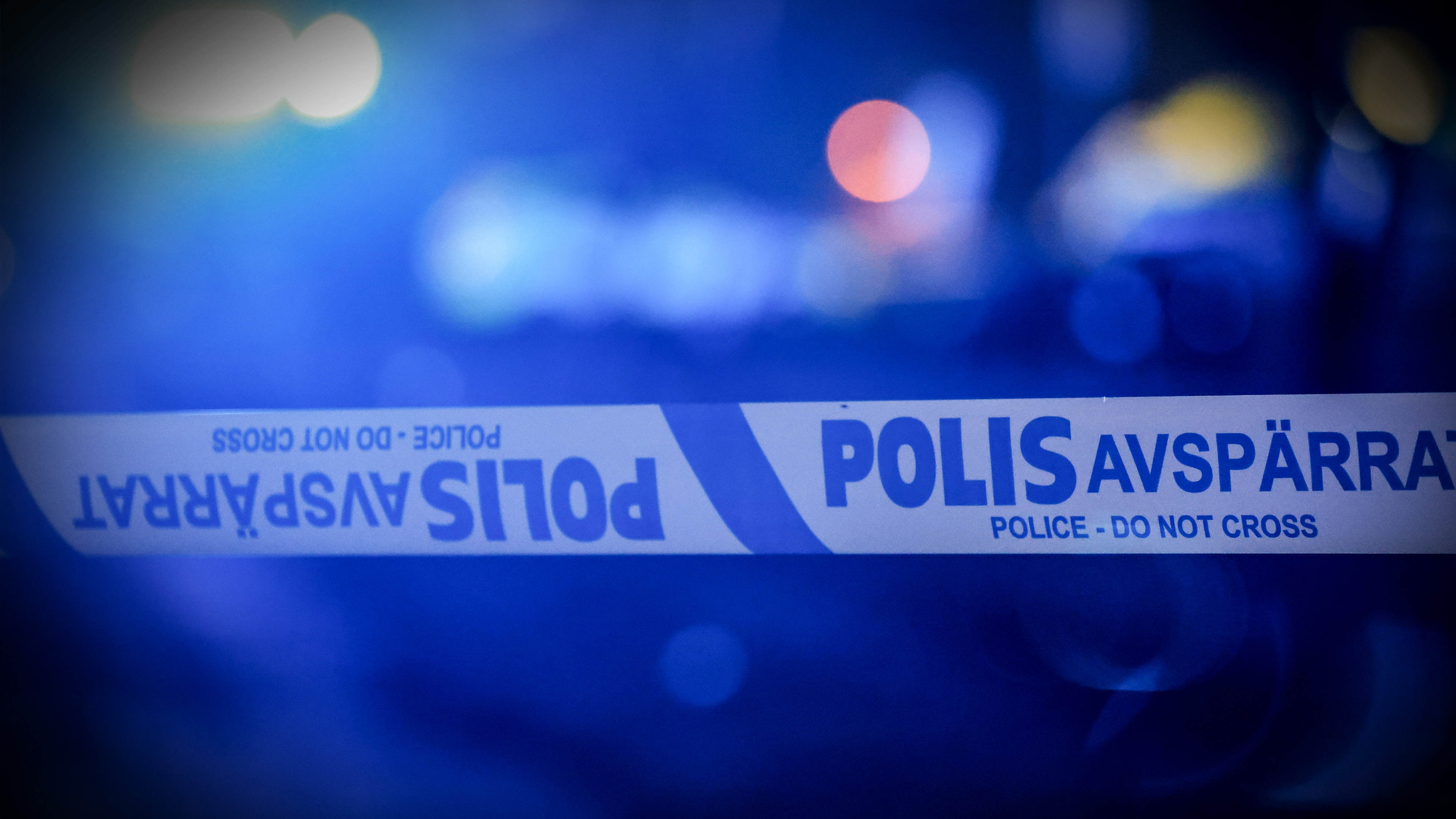Närbild på svensk polisavspärrningstejp med texten "POLIS AVSPÄRRAT" och "POLICE - DO NOT CROSS" mot suddig bakgrund.