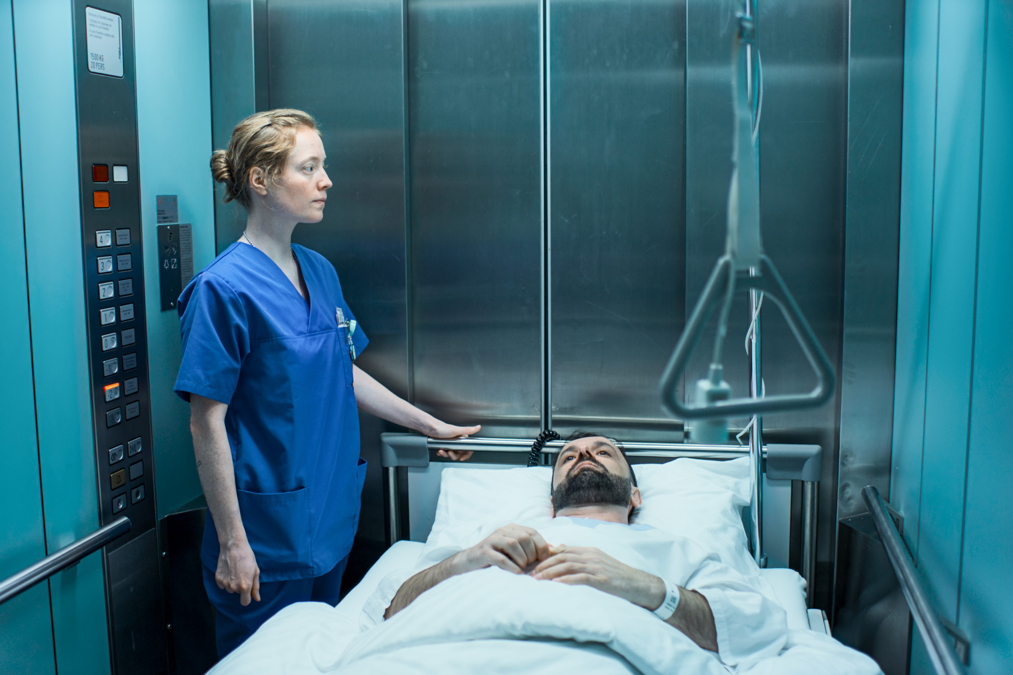 En sjuksköterska står bredvid en patient som ligger i en sjukhussäng inne i en hiss.