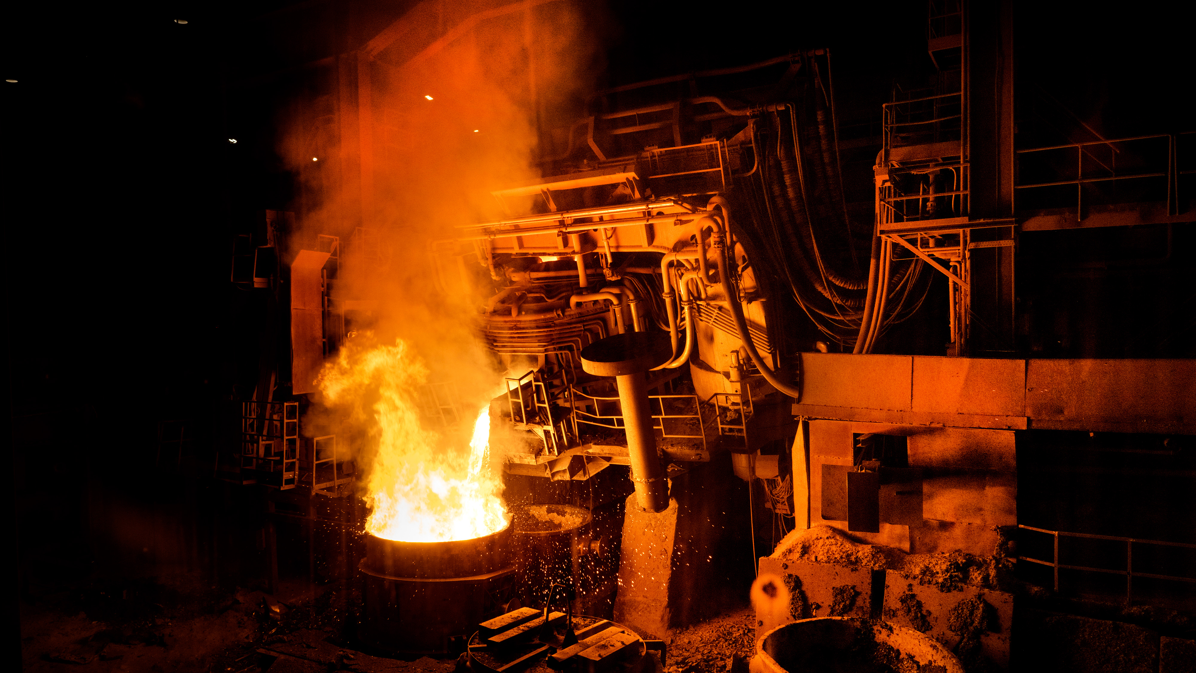 En stor industriugn häller smält metall, vilket ger upphov till lågor och gnistor i en stålverksanläggning.