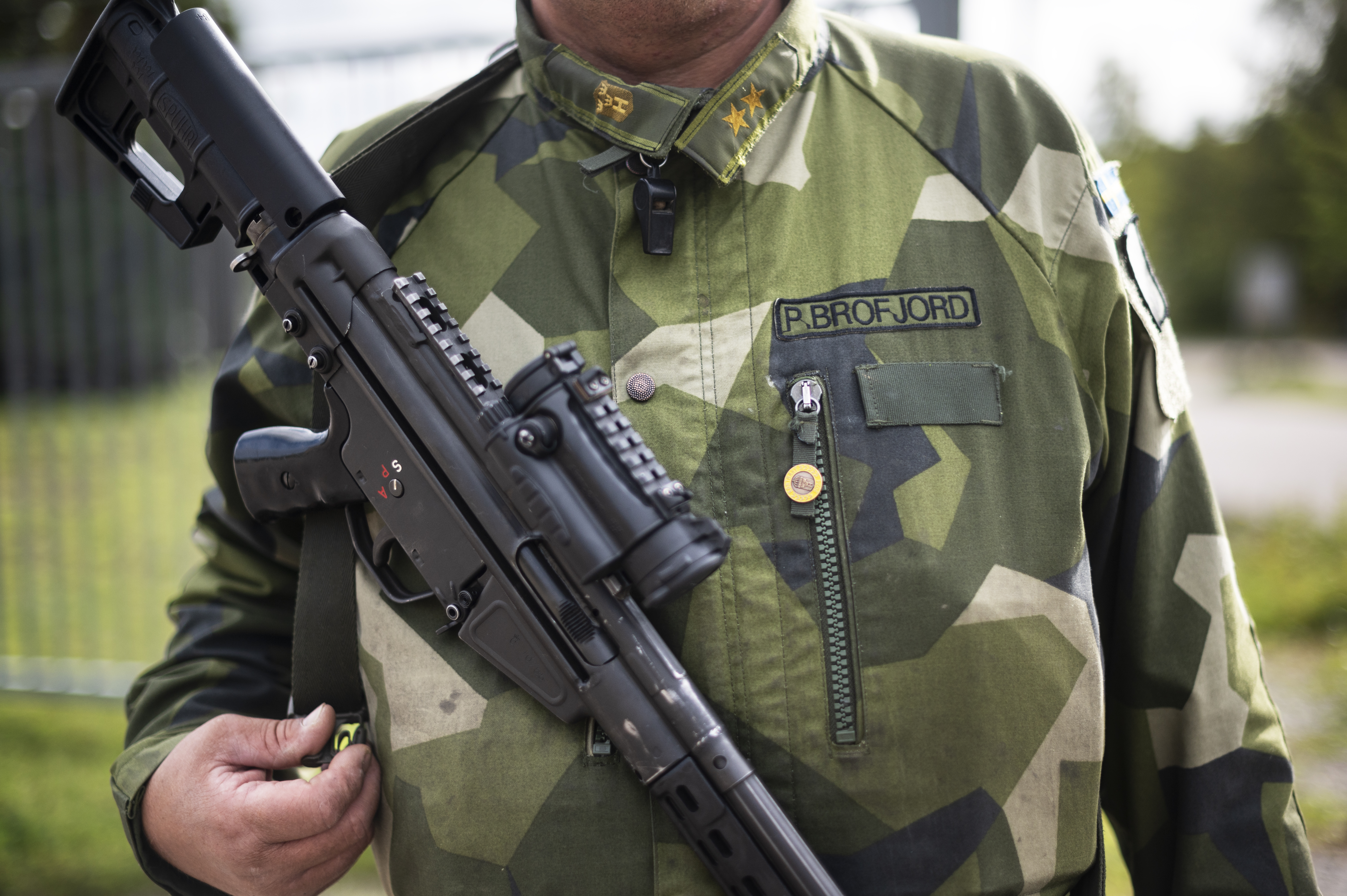 En person i militäruniform med grönt kamouflagemönster håller ett svart automatgevär.