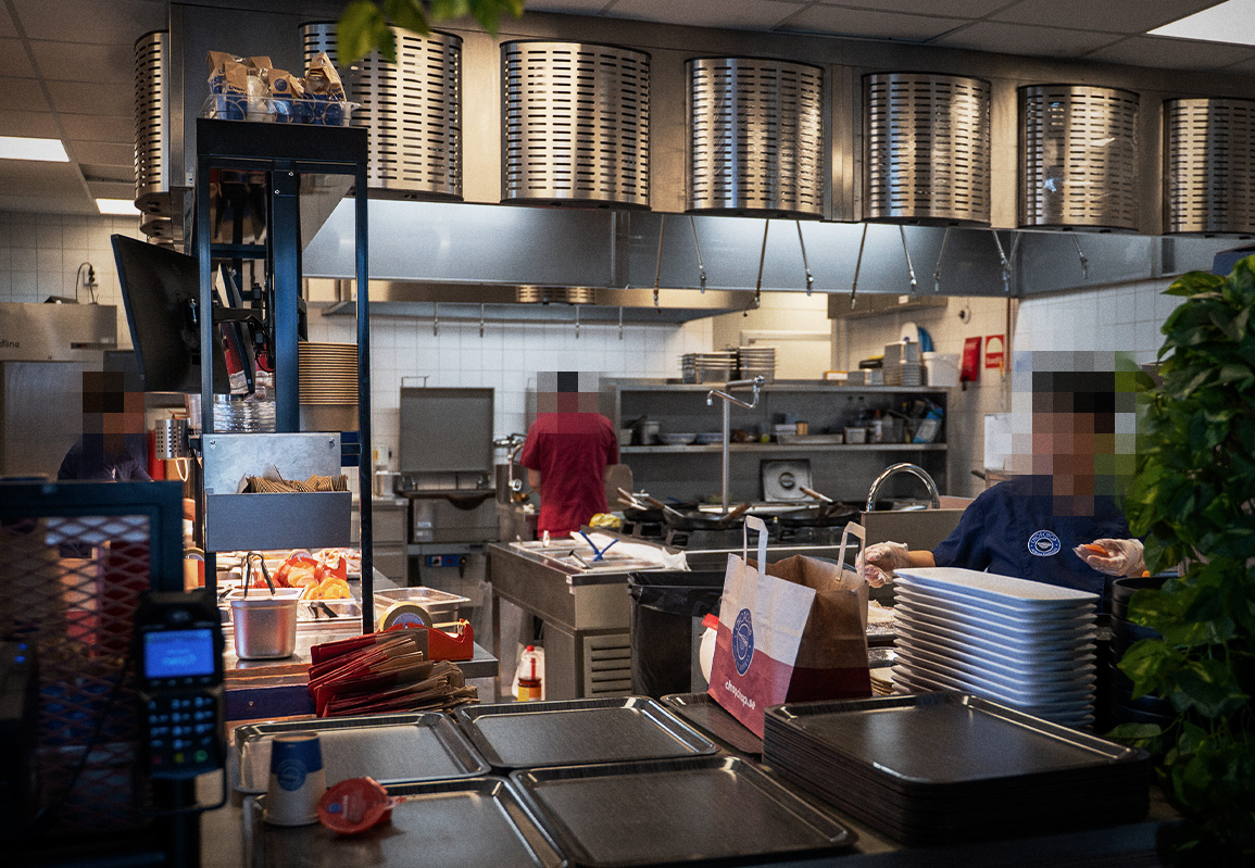 Ett storkök där personal lagar mat samt redskap, utrustning och beställningar på bänkarna.