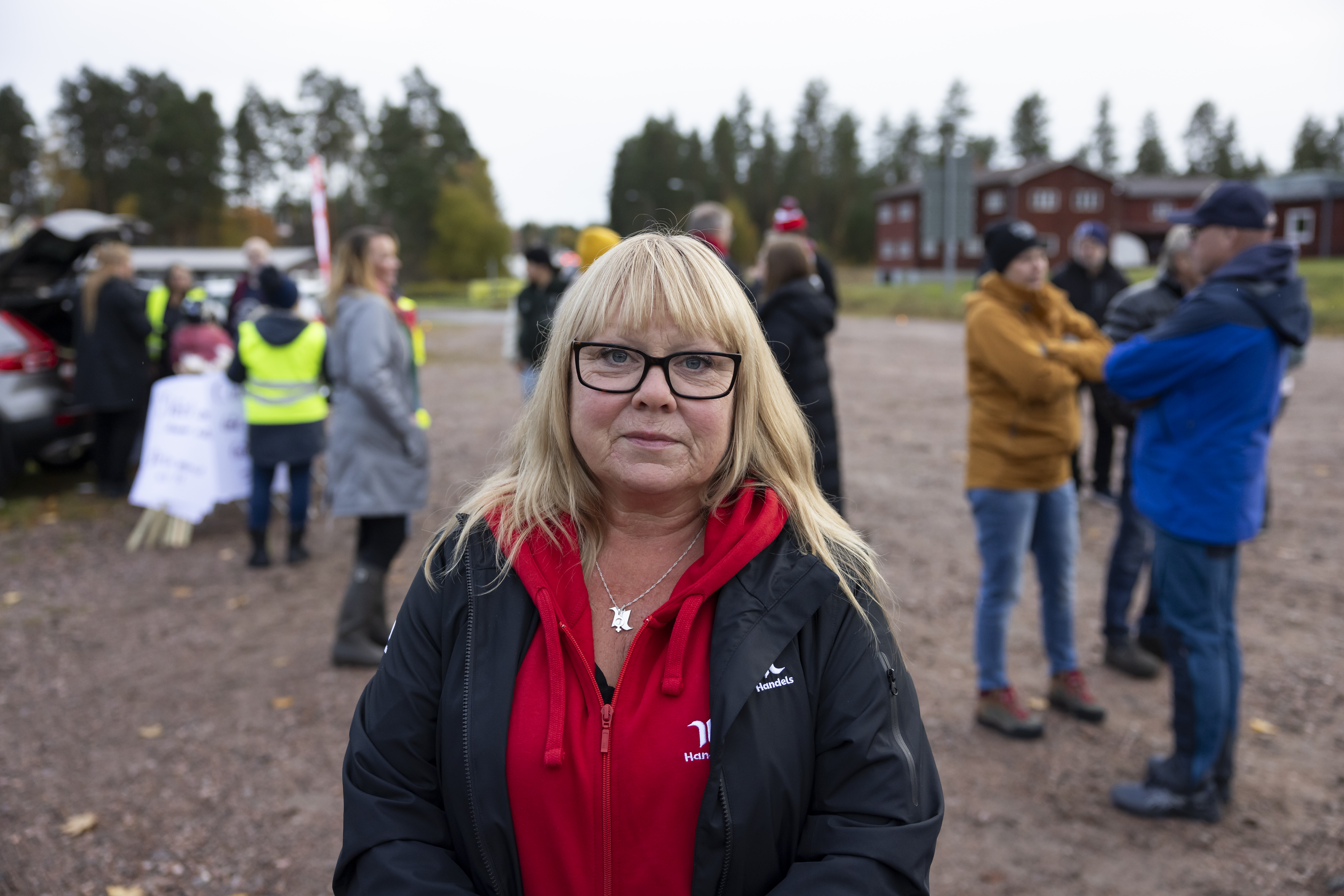 Ljushårig kvinna med röd tröja och svart jacka, samt glasögon.
