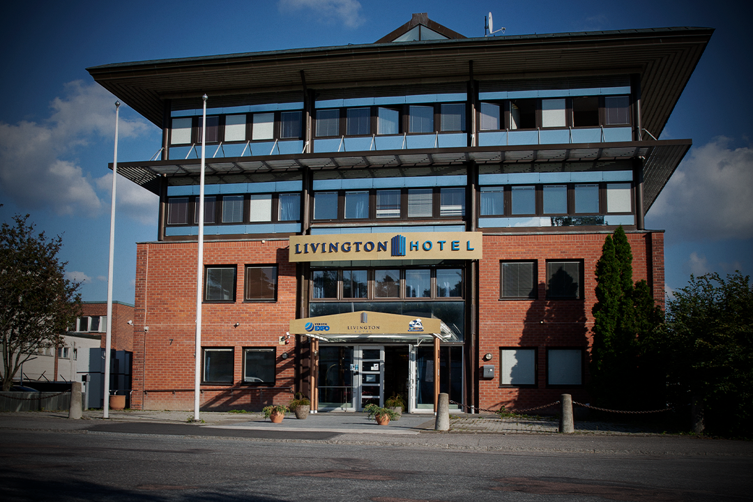 En byggnad i tre våningar av tegel och glas med en skylt där det står "Livington Hotel", två flaggstänger och krukväxter vid ingången.