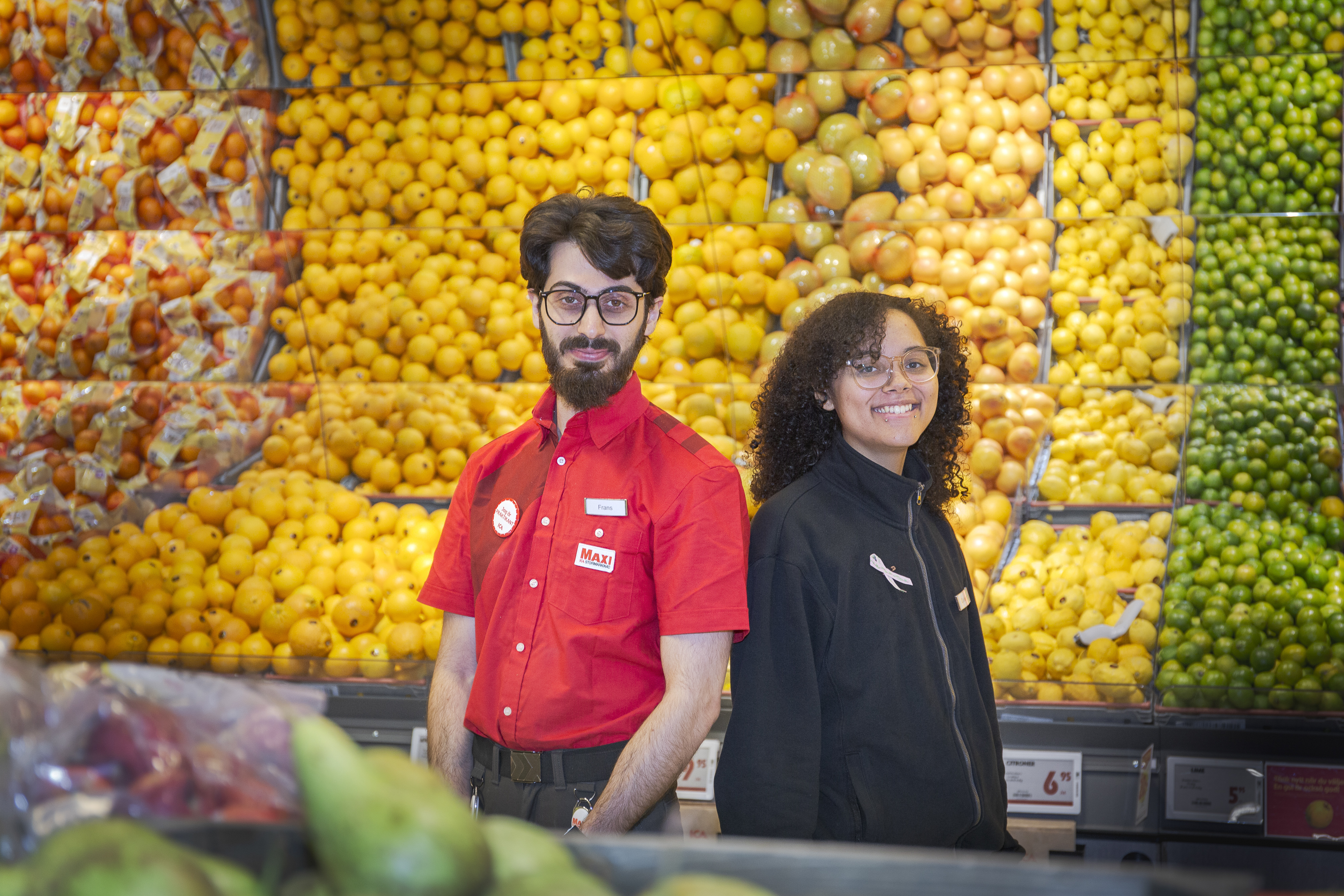 Två butiksanställda står framför ett fruktbord med citroner, apelsiner och grapefrukter.