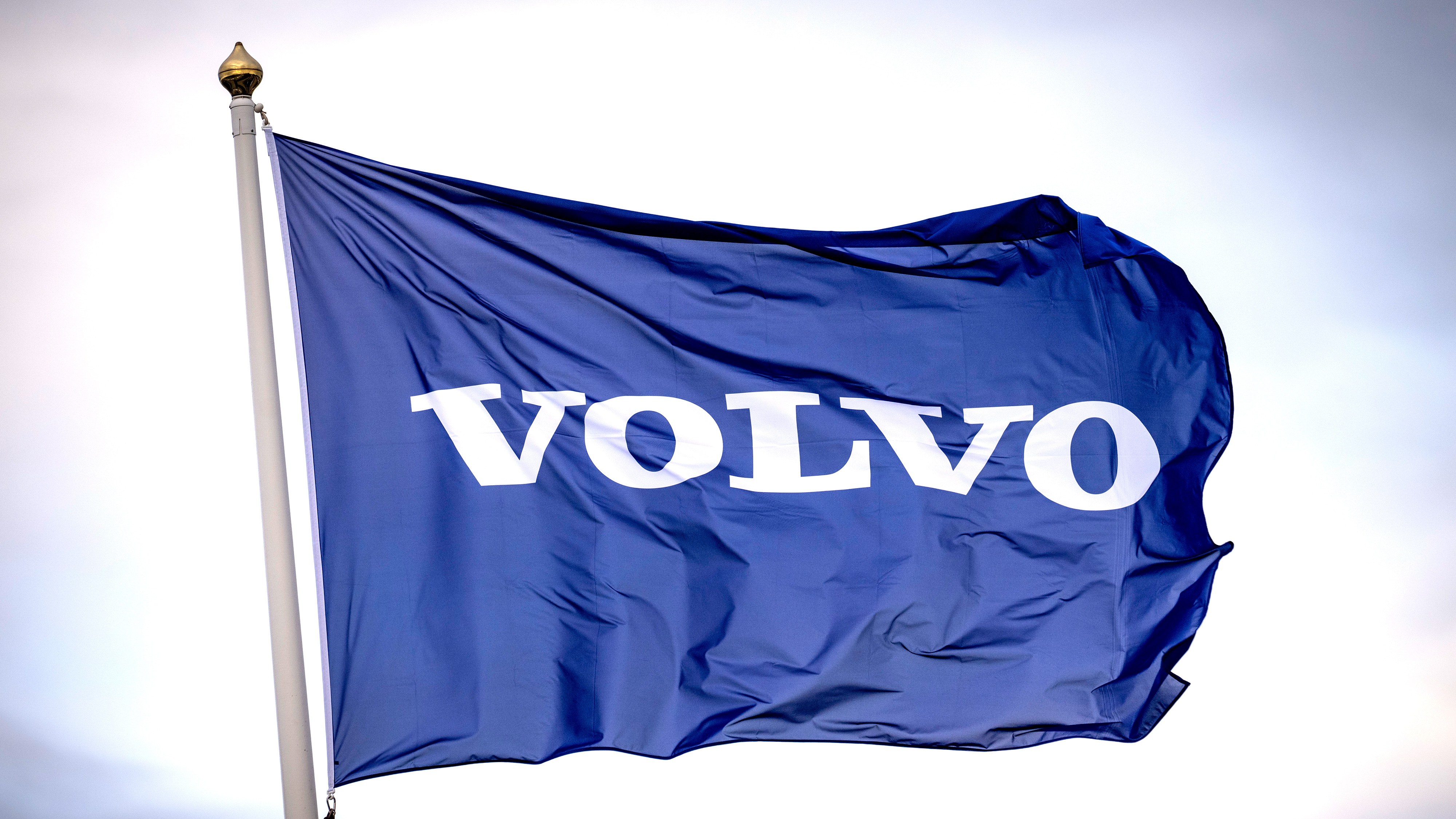 Blå flagga med ordet "VOLVO" i vita versaler, hissad på en flaggstång mot en himmel med moln.