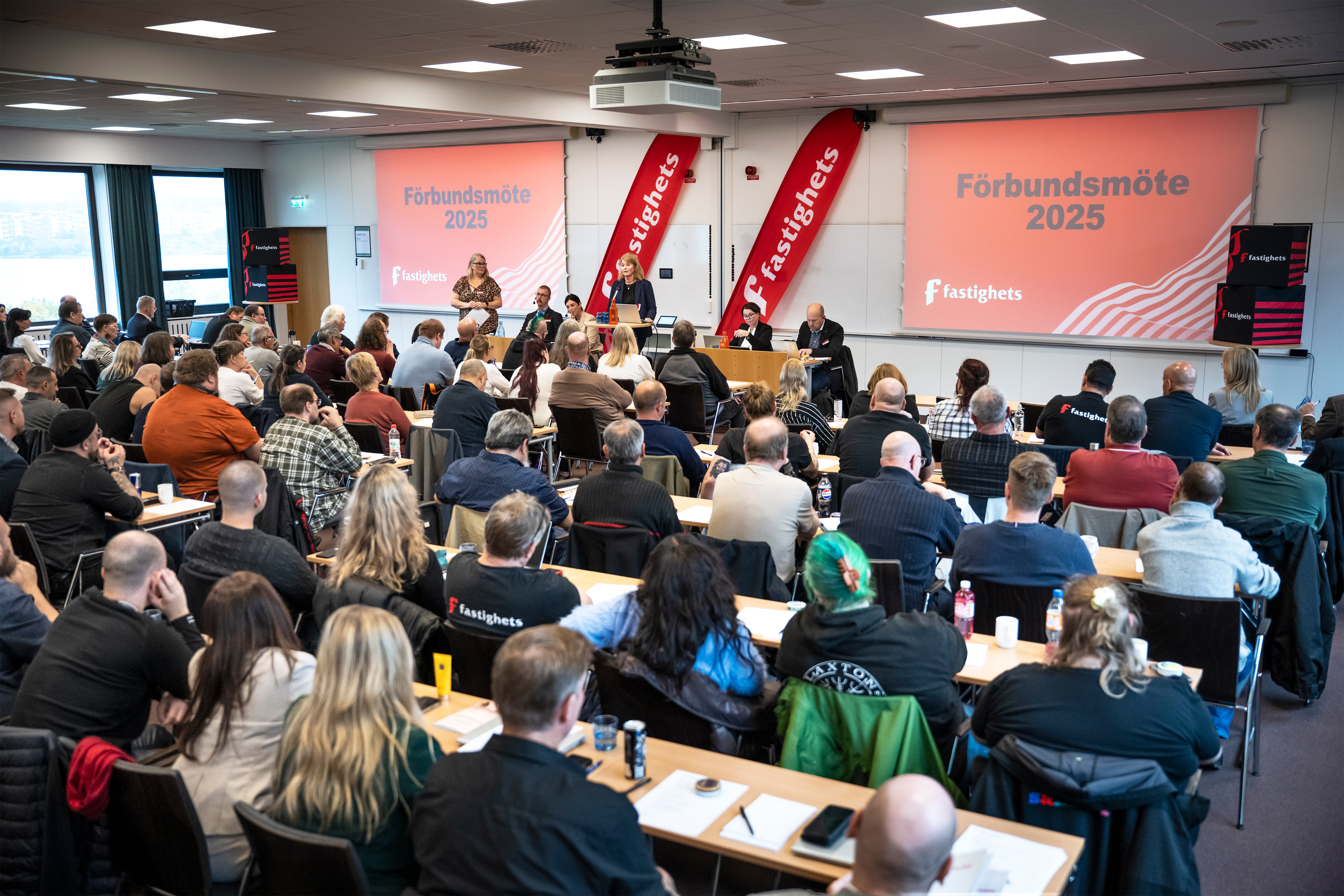 Ombud från Fastighets på stort möte med kvinna i talarstolen.