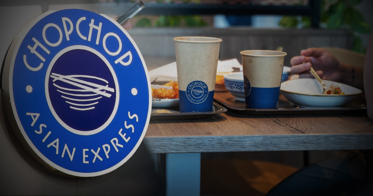 Runt blå skylt med texten "ChopChop Asian Express" bredvid ett bord med brickor, mat, ätpinnar och pappersmuggar i restaurang.