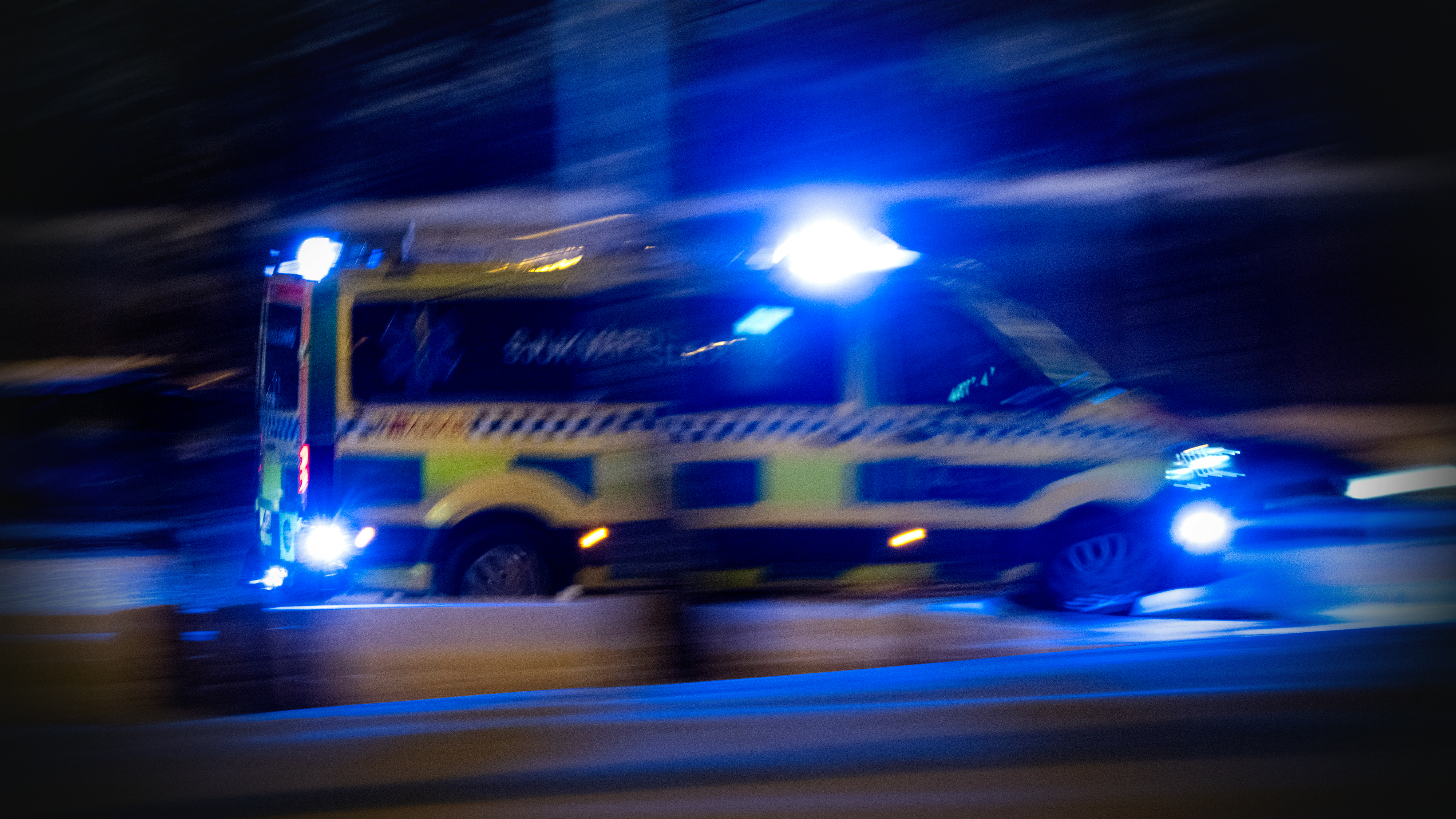 En bild av en ambulans med blåljus som kör på natten.