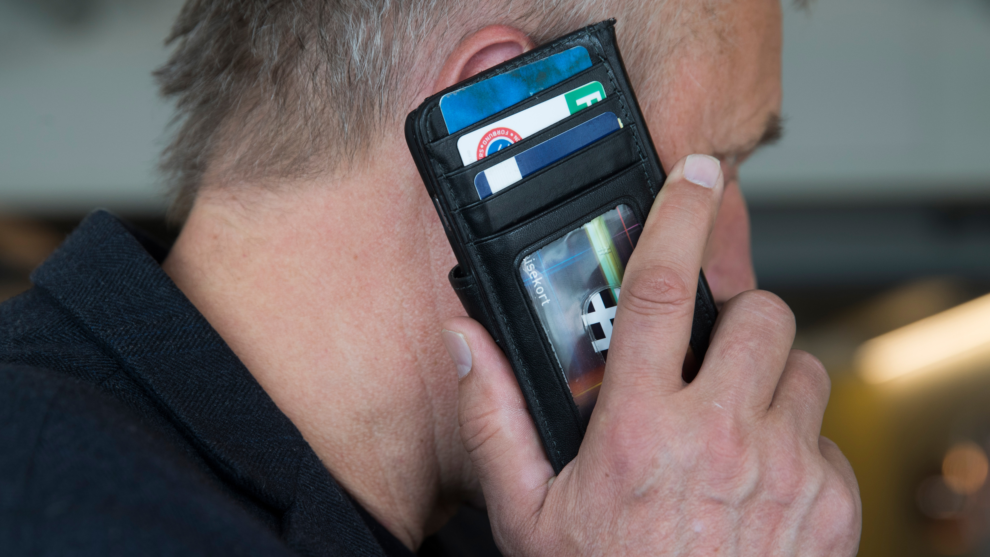 En person håller en öppen plånbok med flera kort mot sitt öra och använder den som en telefon.