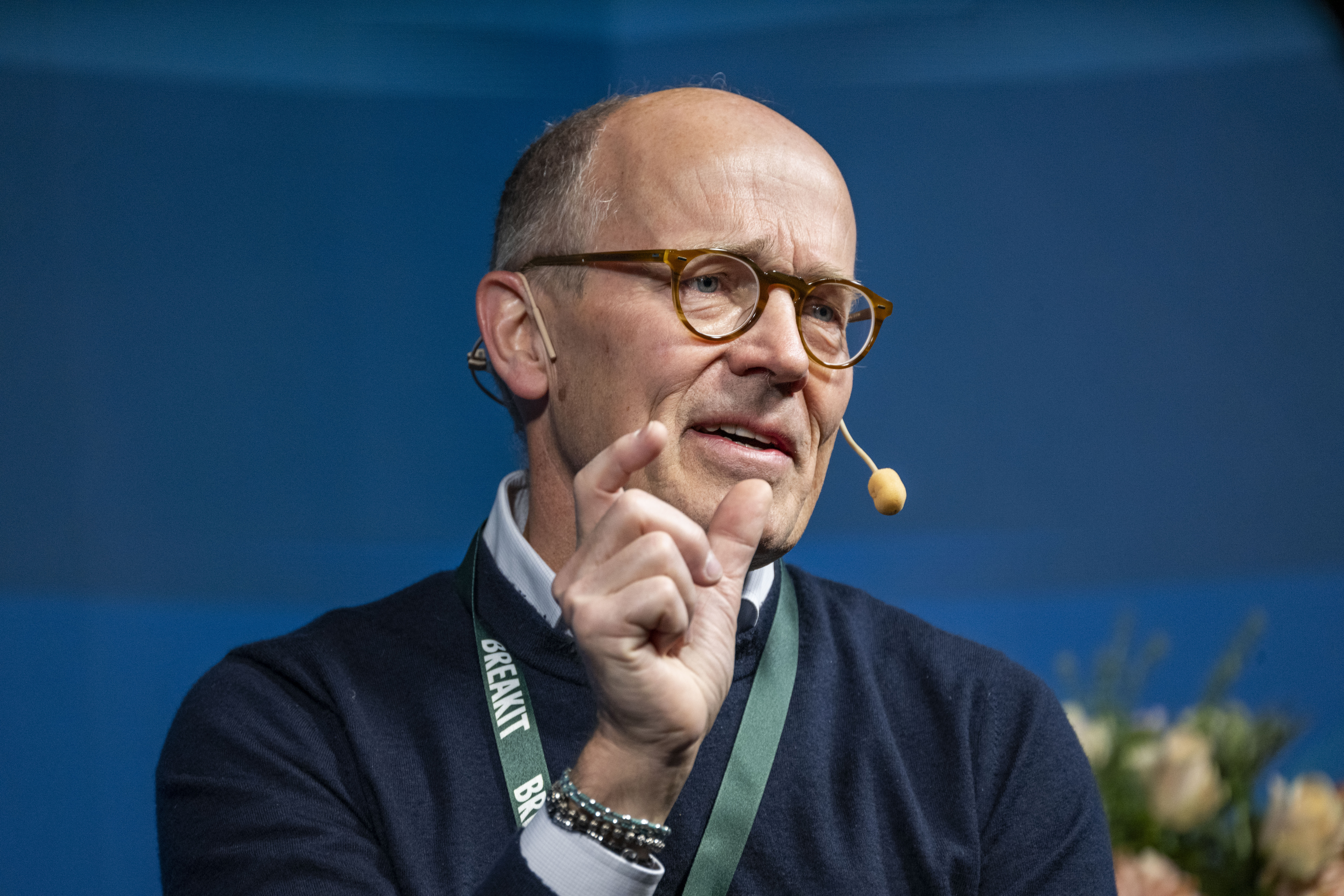 Harald Mix med glasögon och headset-mikrofon gestikulerar med handen och talar framför en blå bakgrund.