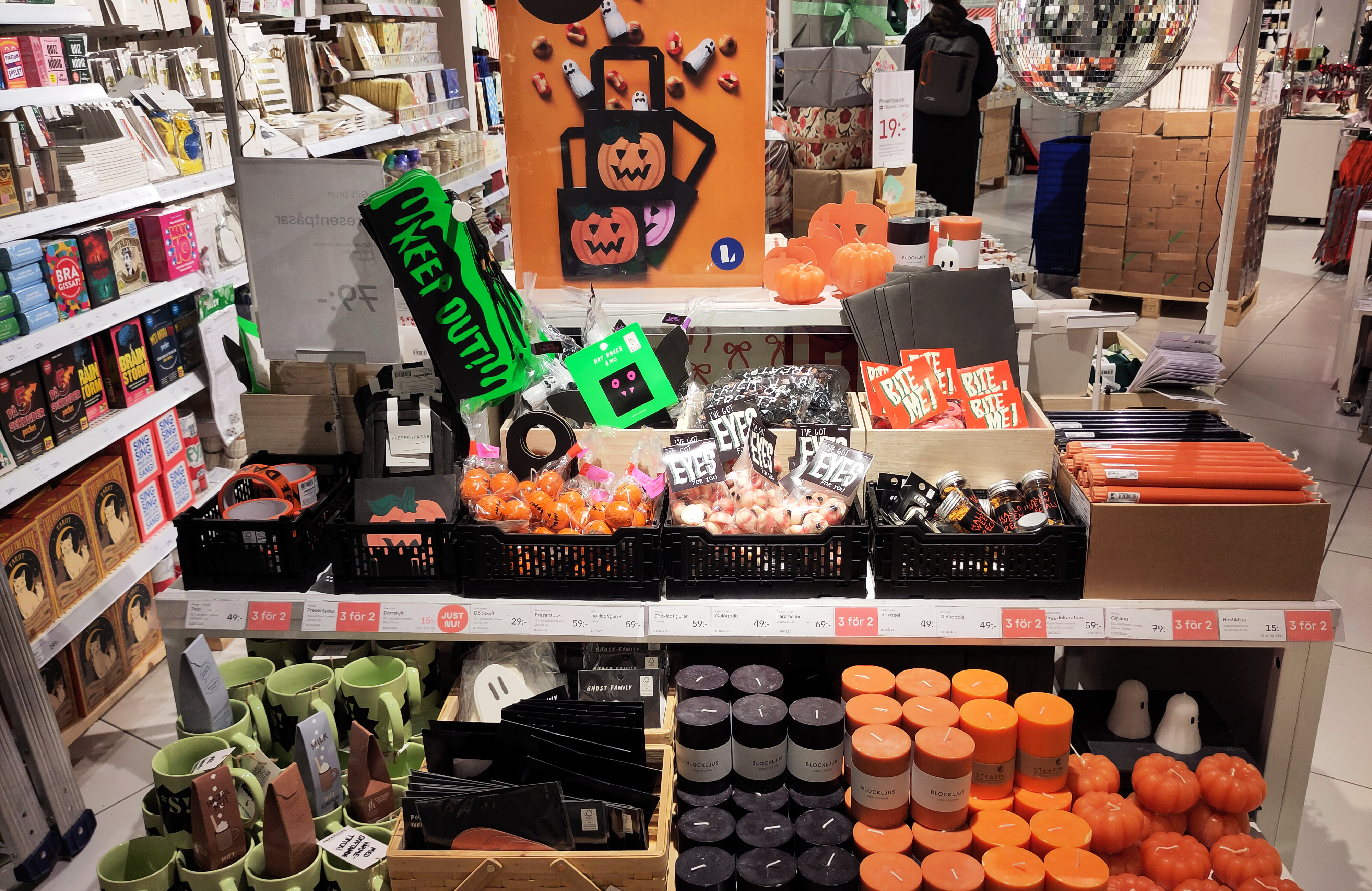 En butikshylla visar halloweensaker som pumpor, dekorationer, muggar och tillbehör ordnade på hyllor och bord.