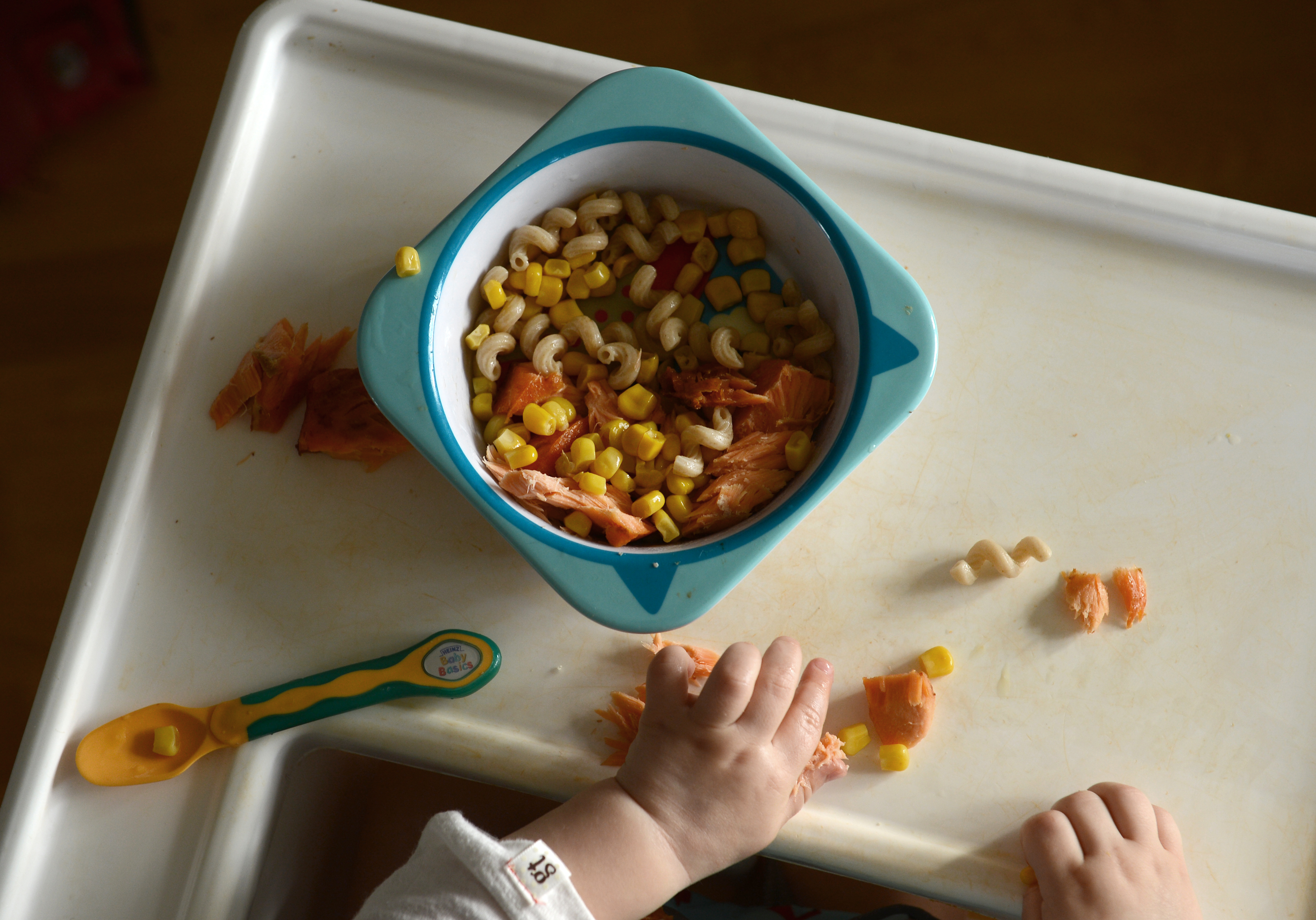 En bebis äter lunch med händerna. Lax och pasta och mycket kladd.