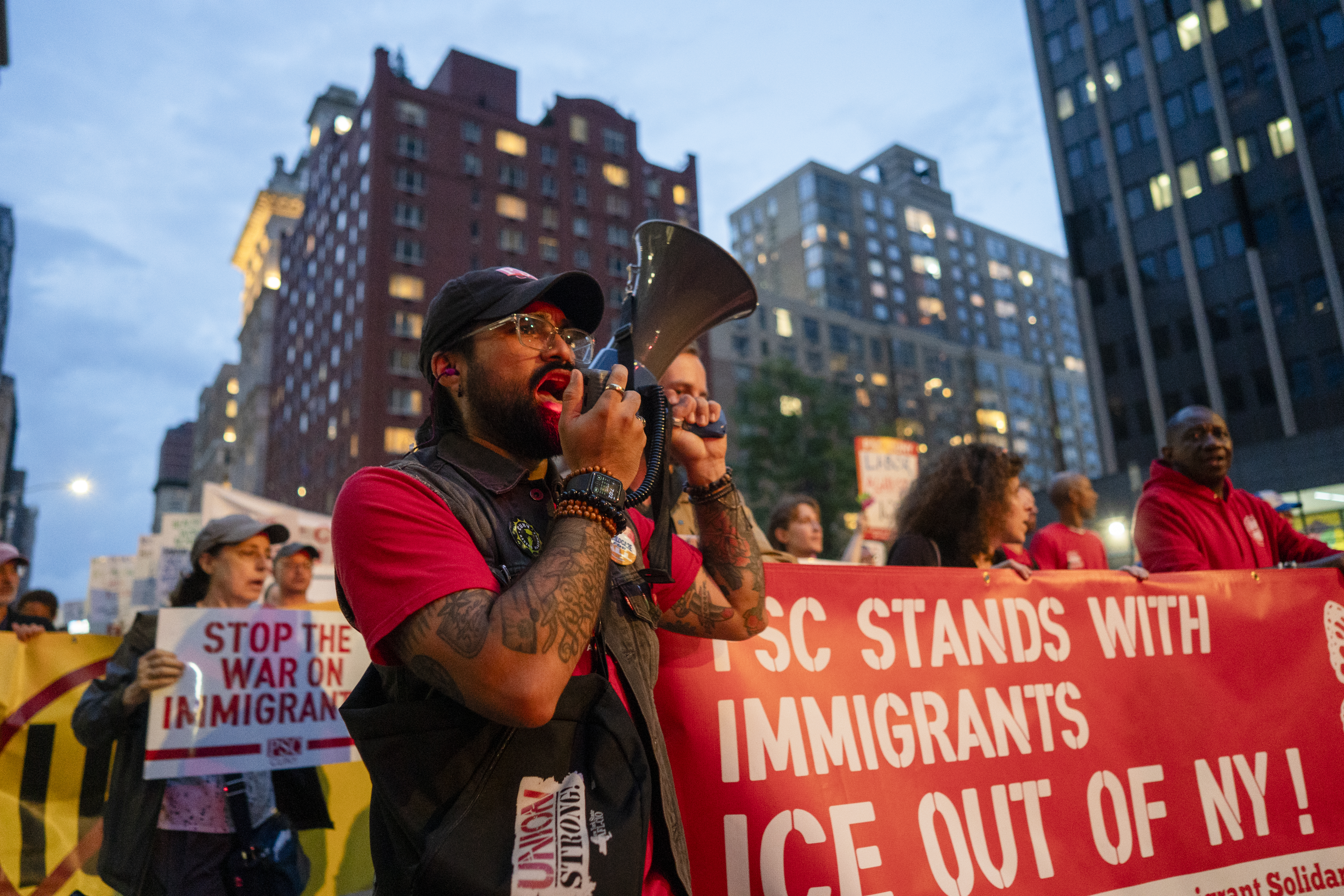 Demonstranten Arturo talar i en megafon på en migrationsdemonstration i New York, med skyltar som stödjer migranter och ber ICE lämna.