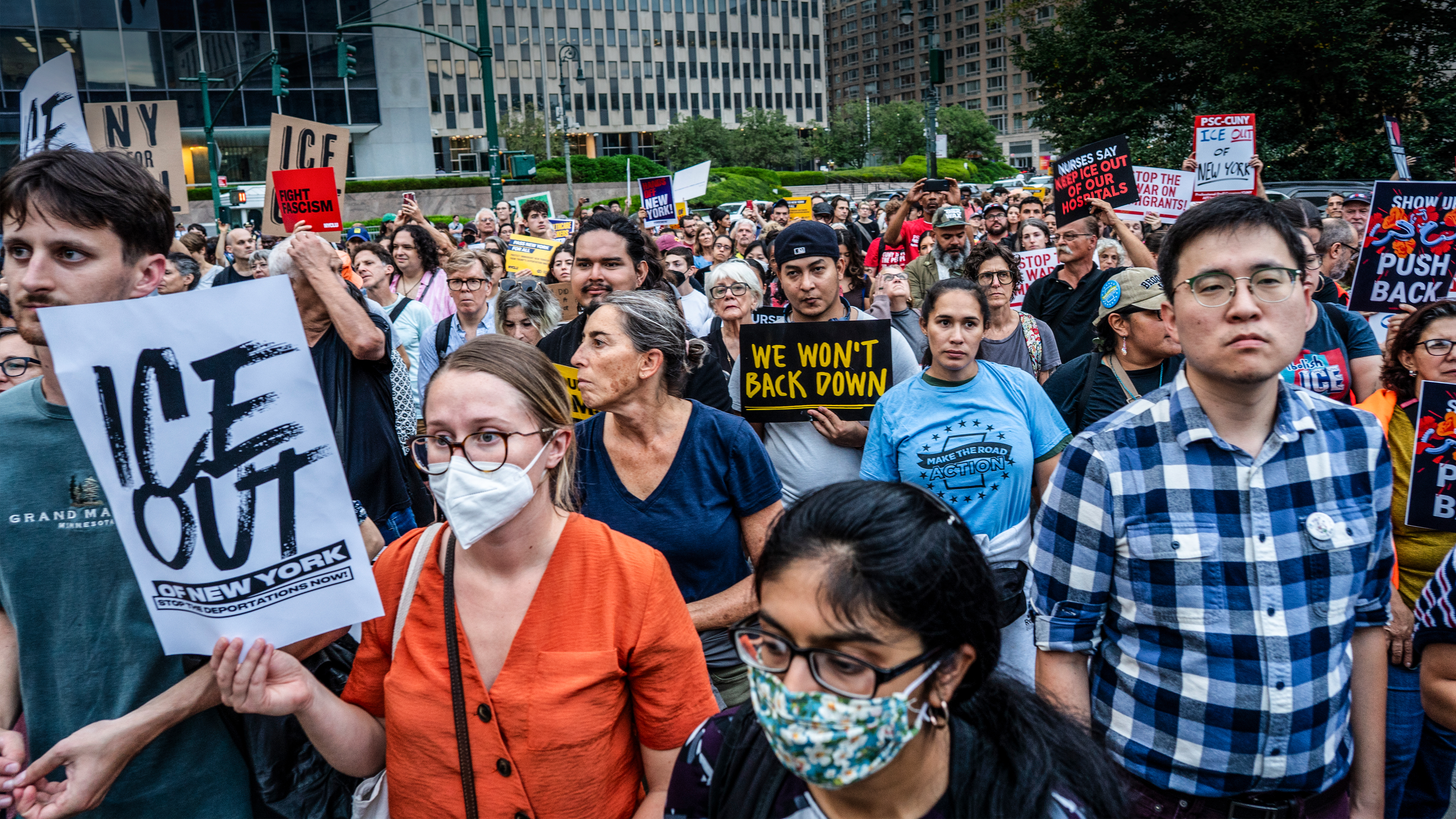 En folkmassa demonstranter håller upp skyltar där det står "ICE Out of New York" och "We Won't Back Down" i en stadsmiljö.